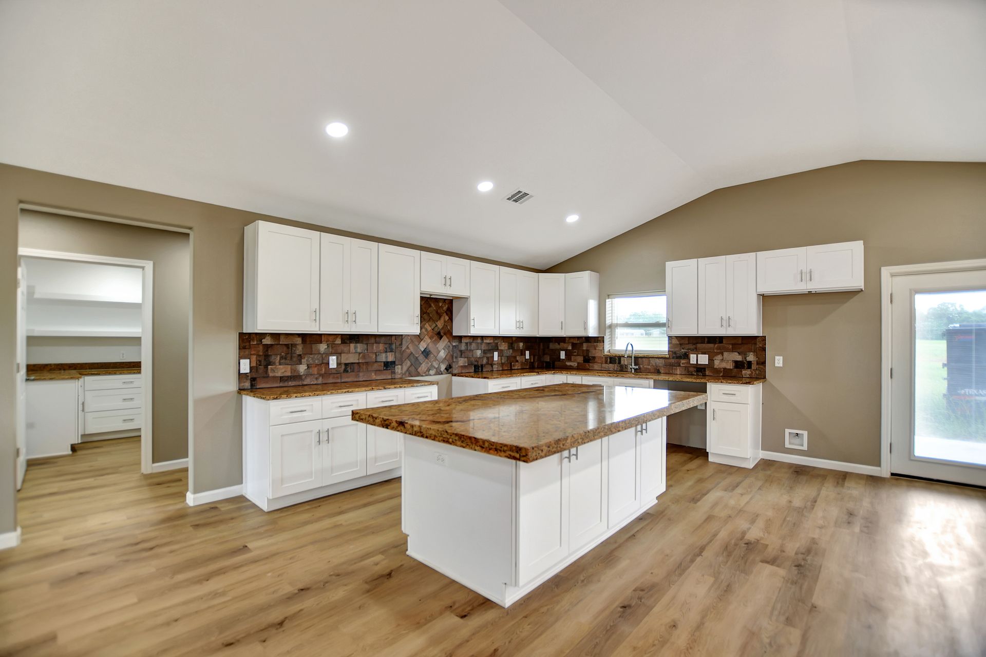 Bright kitchen with white cabinets, brown island, and light wood floors.