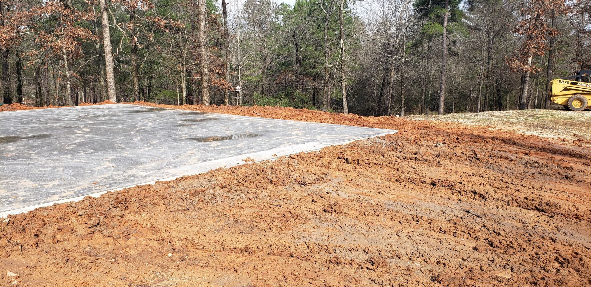 A construction site with a concrete foundation, surrounded by dirt and trees.
