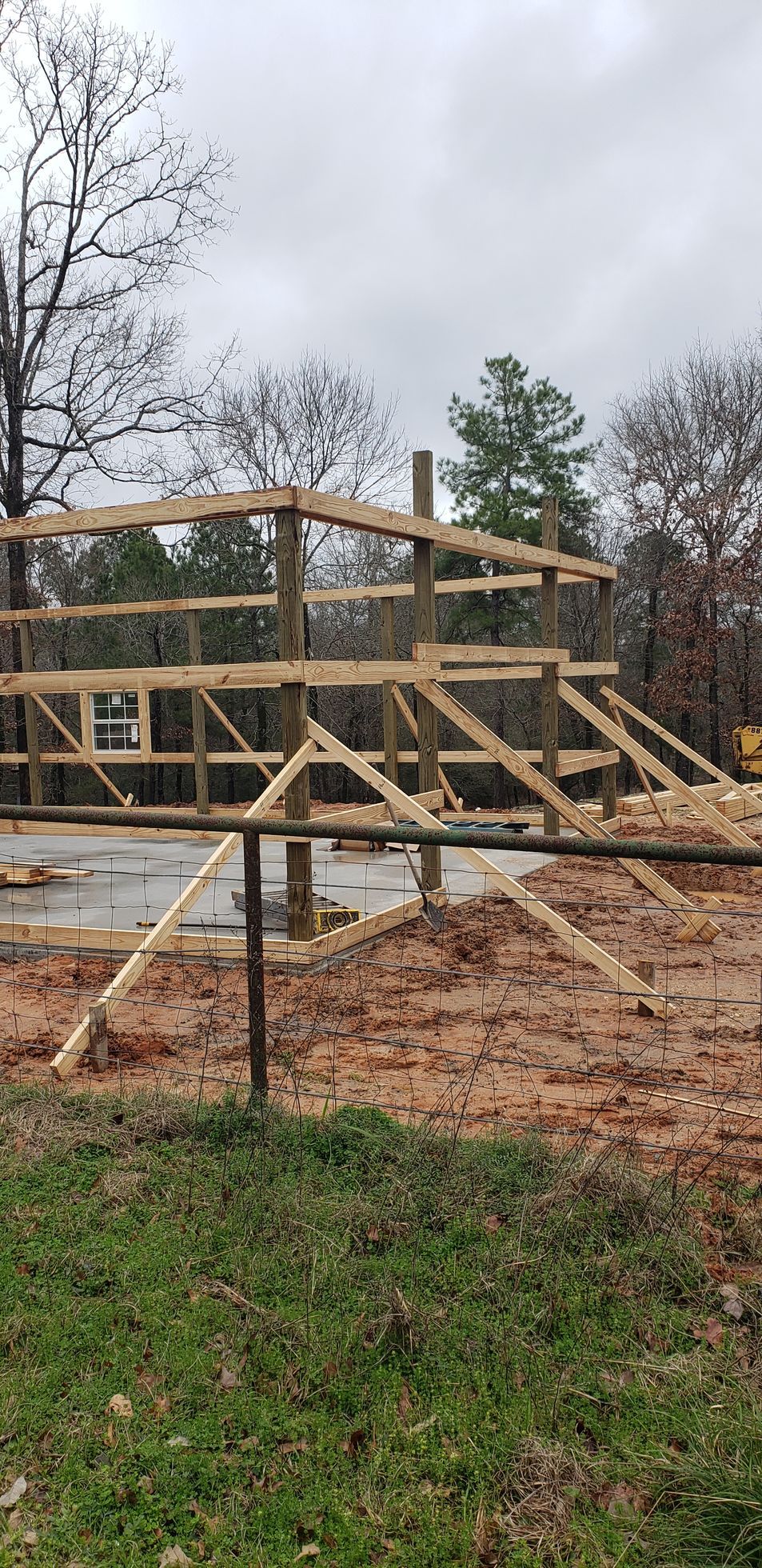 Wooden frame of a building under construction against a cloudy sky, on a muddy lot.