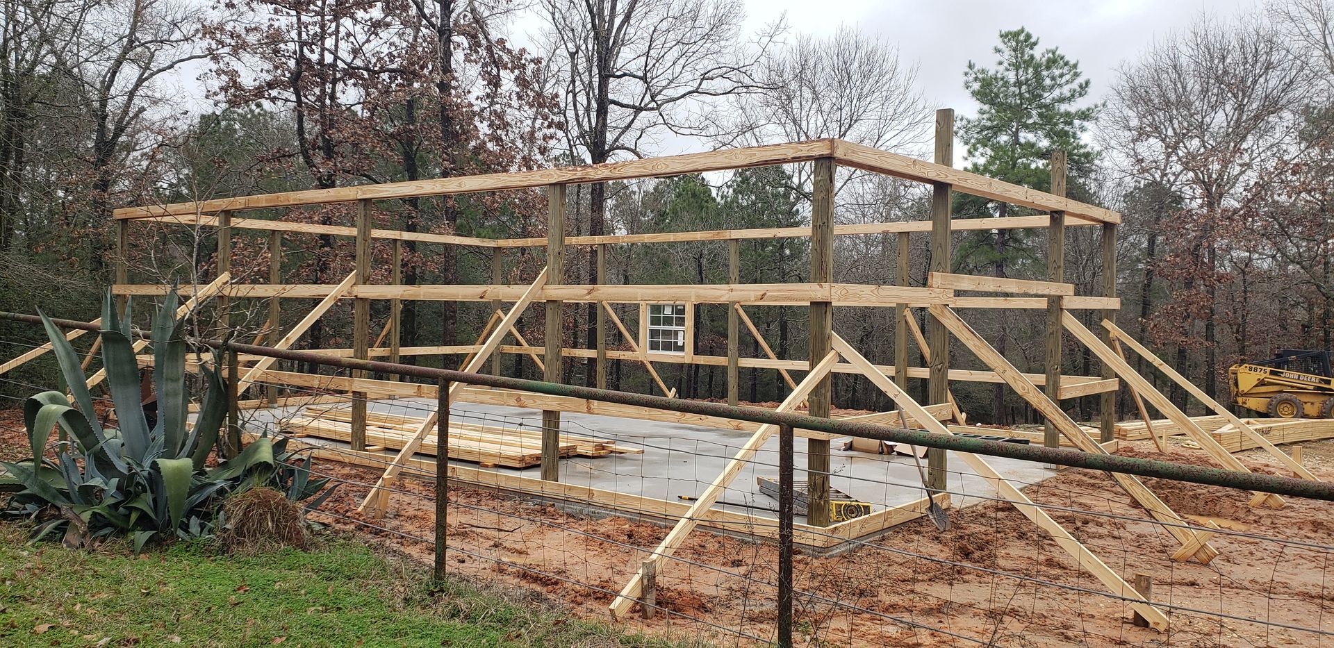 Wooden structure under construction on a dirt lot, surrounded by trees.
