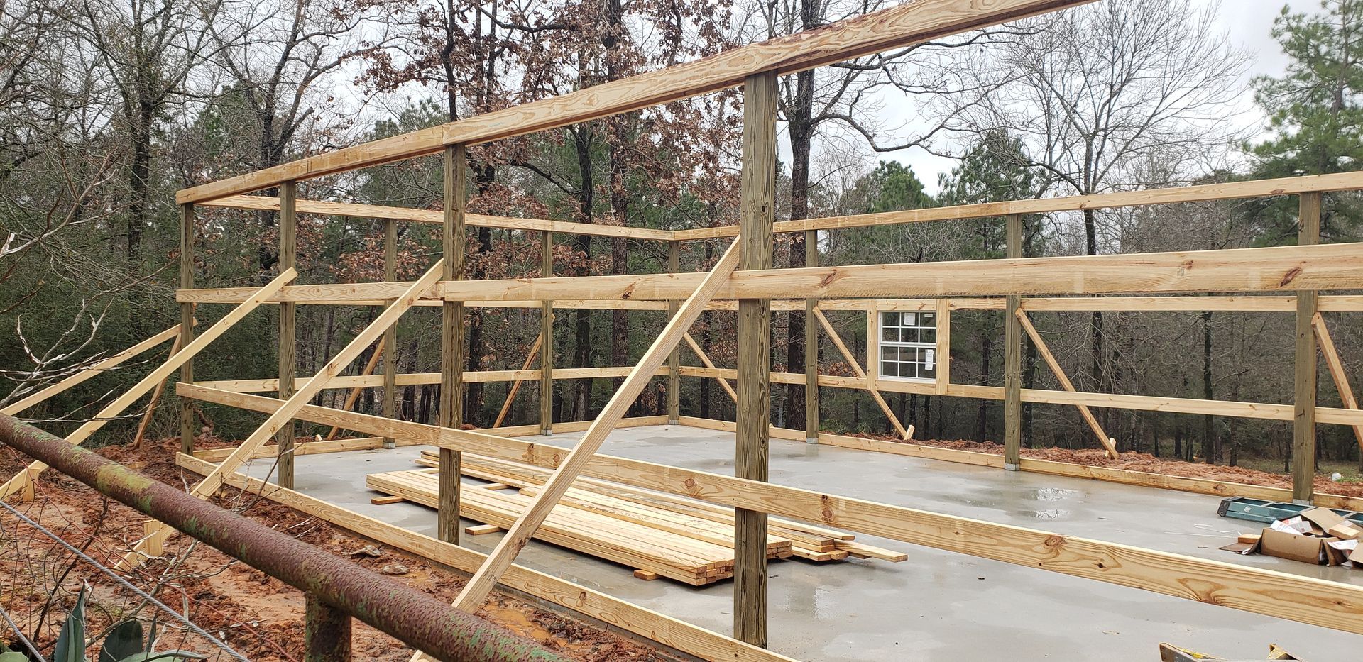 Wooden structure of a building under construction, with a window and lumber on the concrete floor.