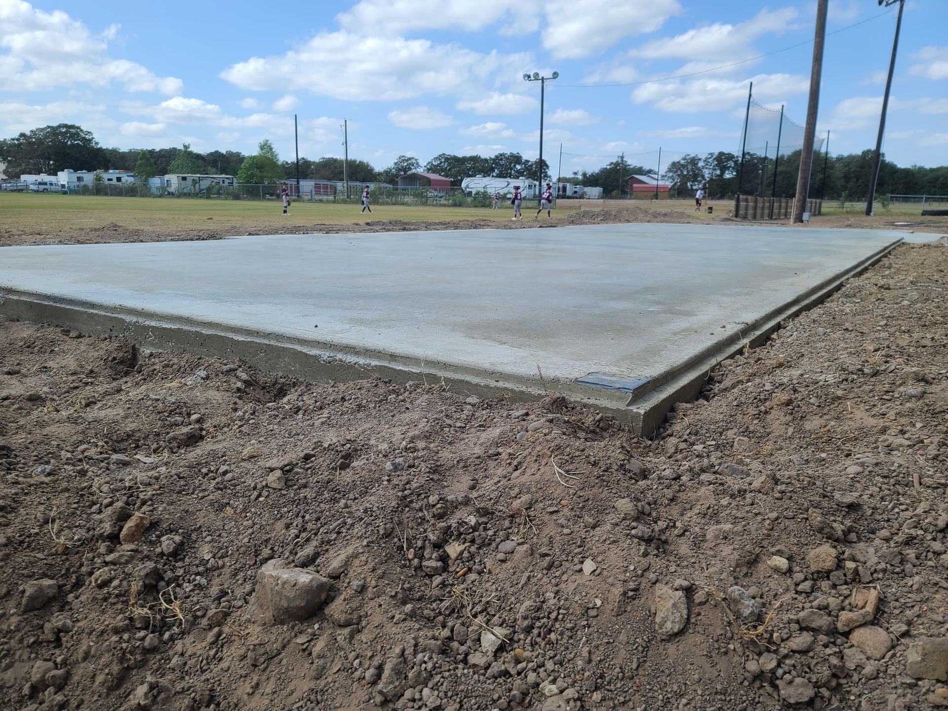 Newly poured concrete slab surrounded by dirt, in an outdoor field setting.