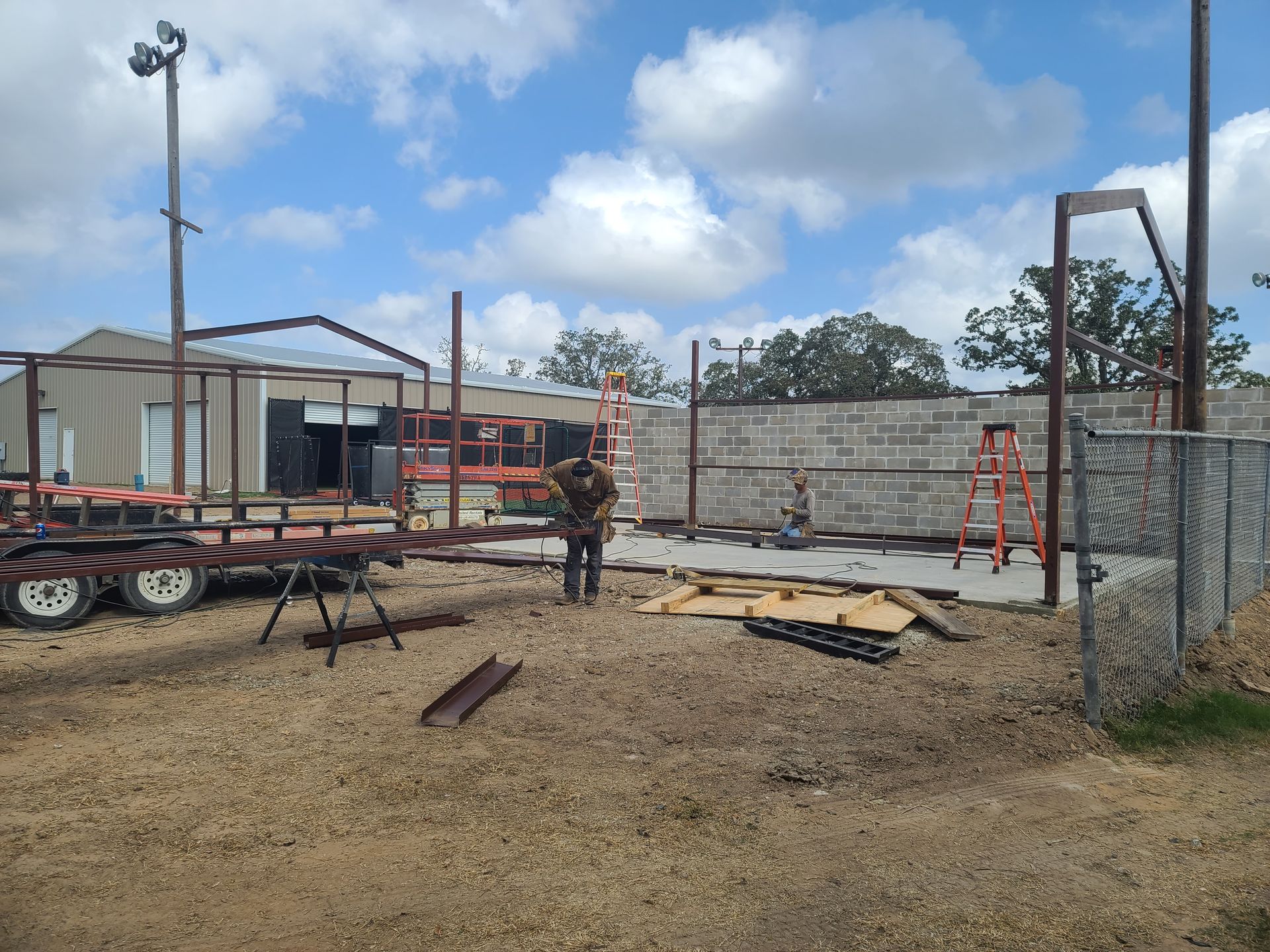 Construction site with a worker and metal framing under a cloudy sky.