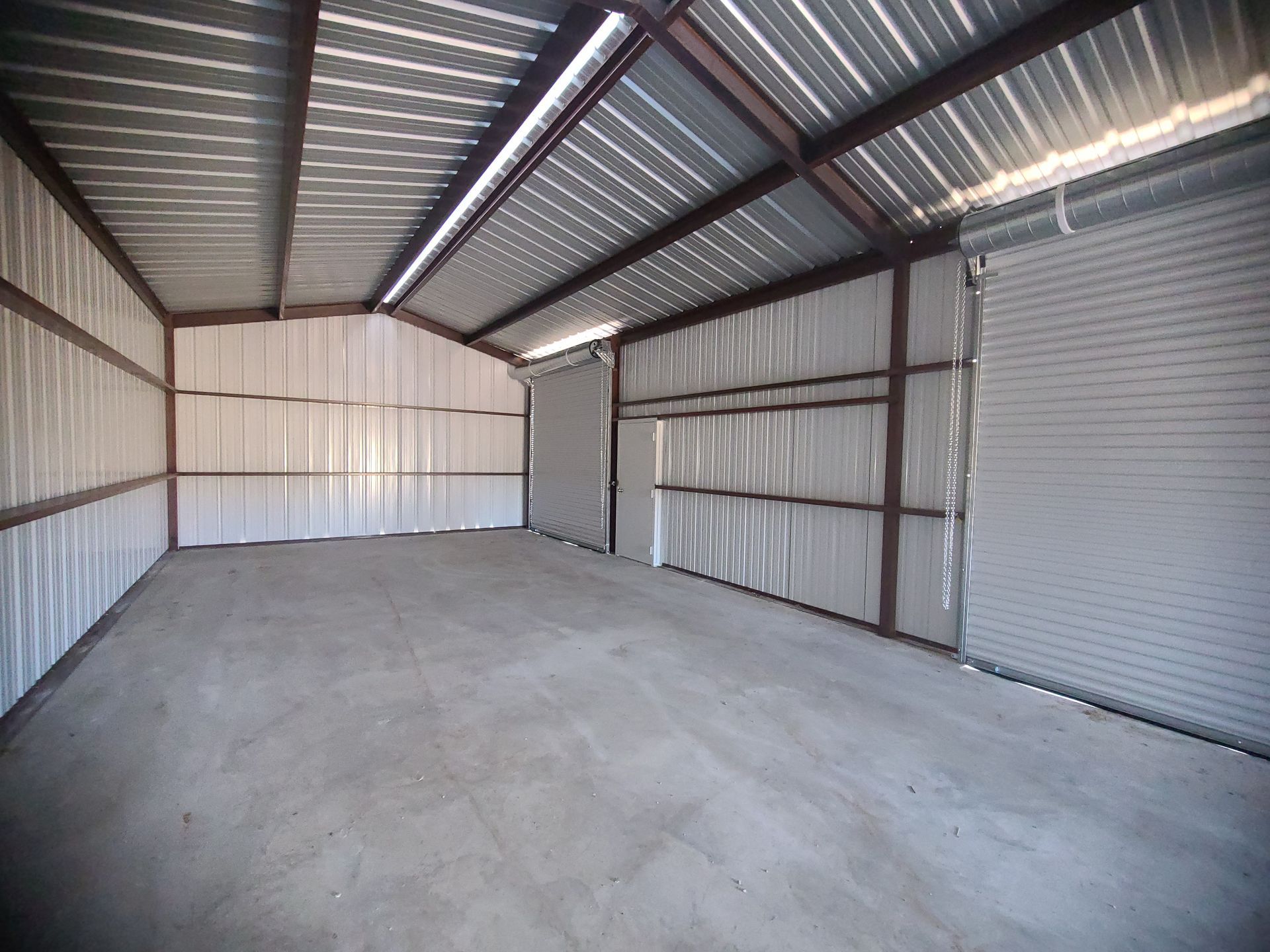 Empty metal storage shed with concrete floor and roll-up door.