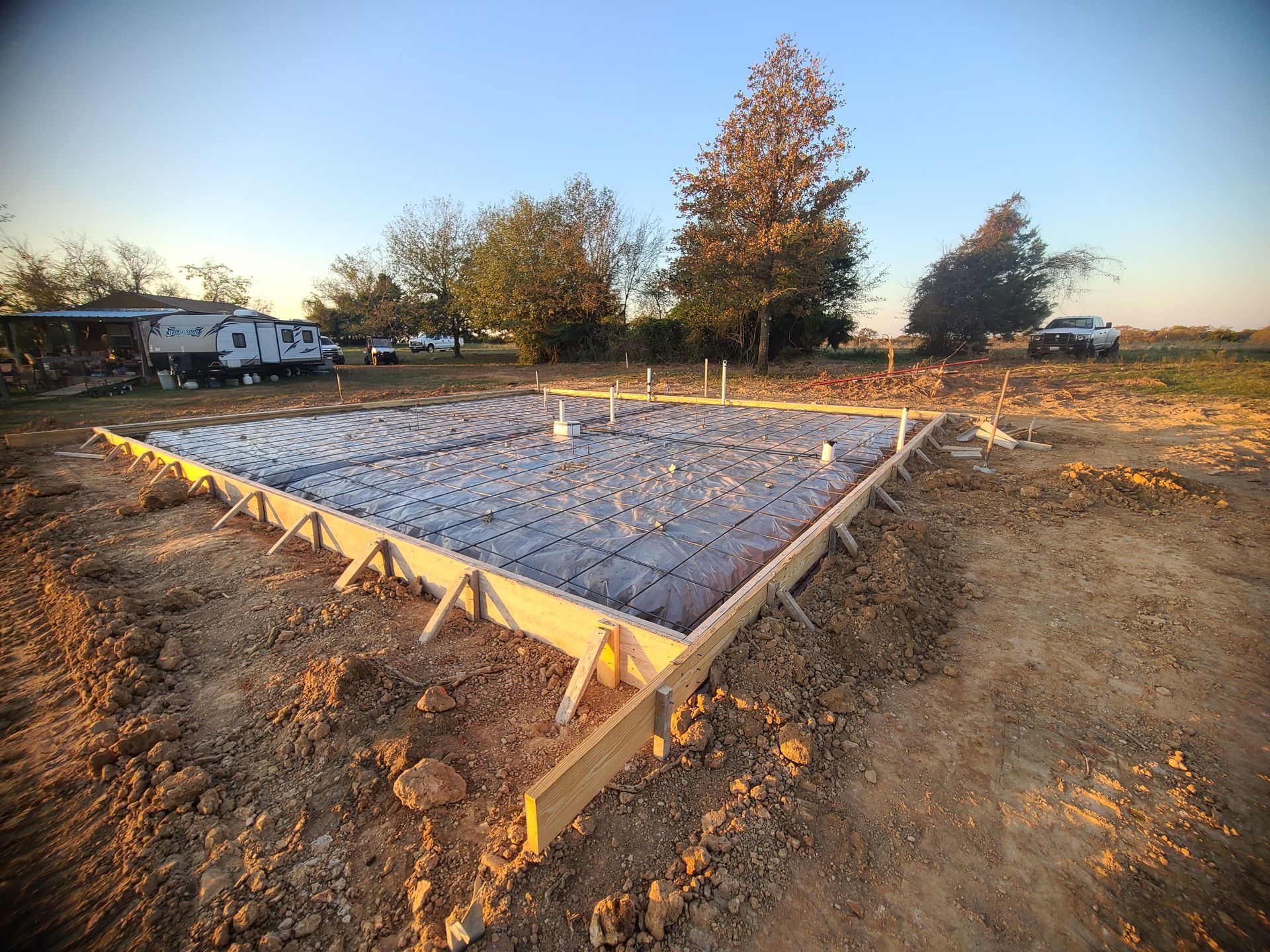 Freshly poured concrete foundation with wooden frame, in a field at sunset.
