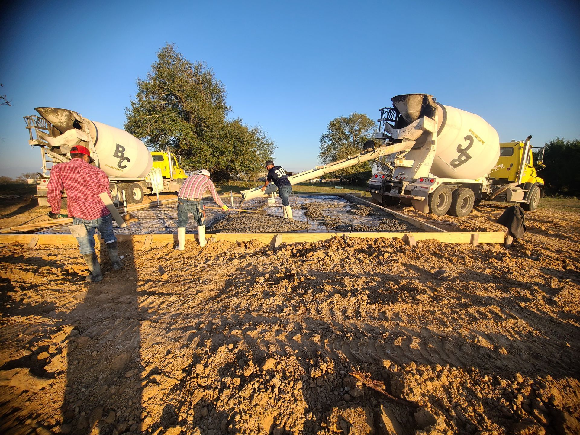Two cement trucks pouring concrete for a foundation, workers in the field.