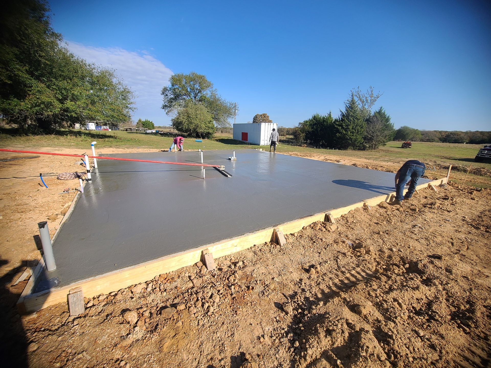 A concrete slab under construction outdoors; a worker smooths the wet concrete.