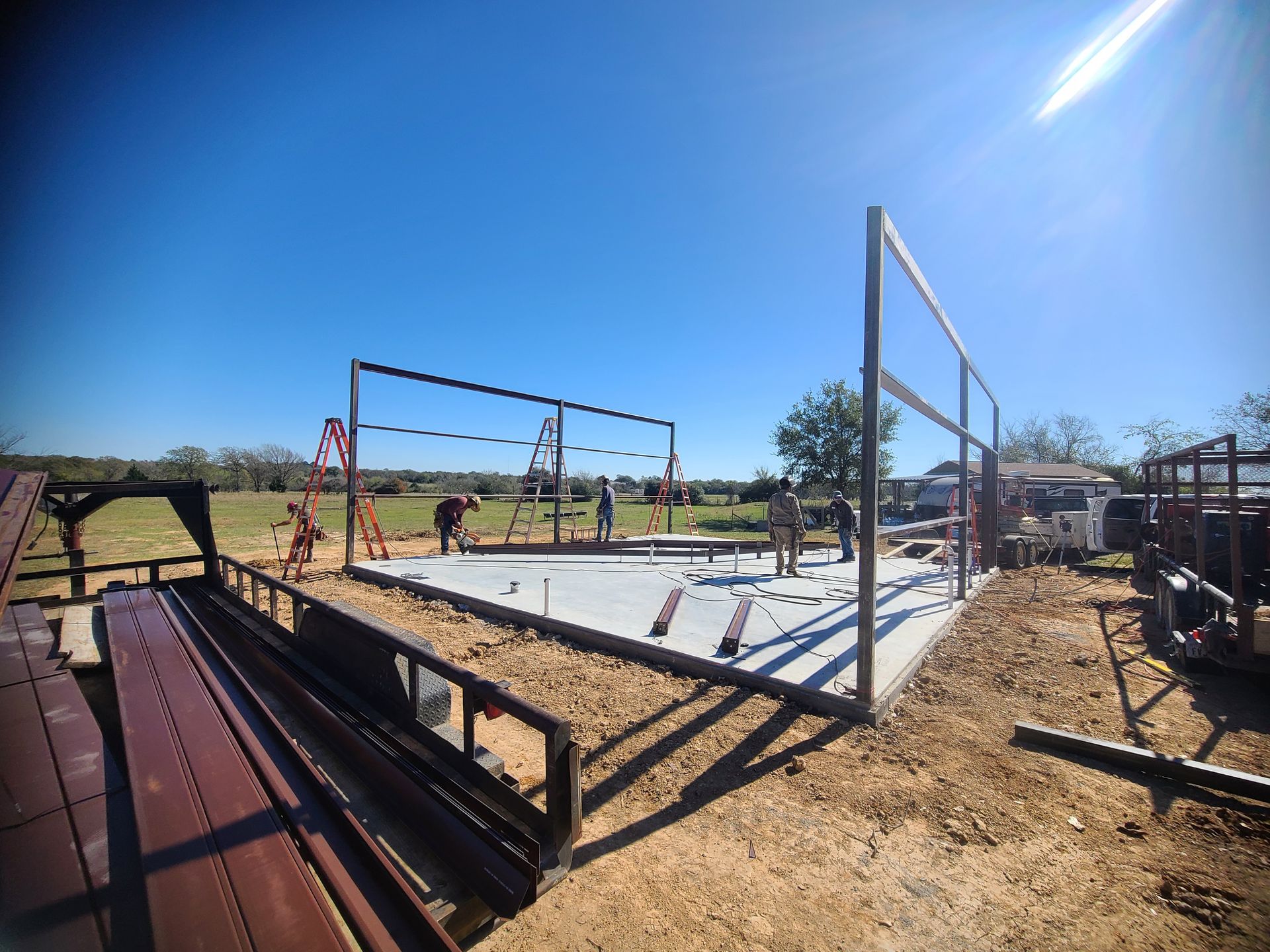 Construction site with metal frame structure under a bright blue sky, workers visible.