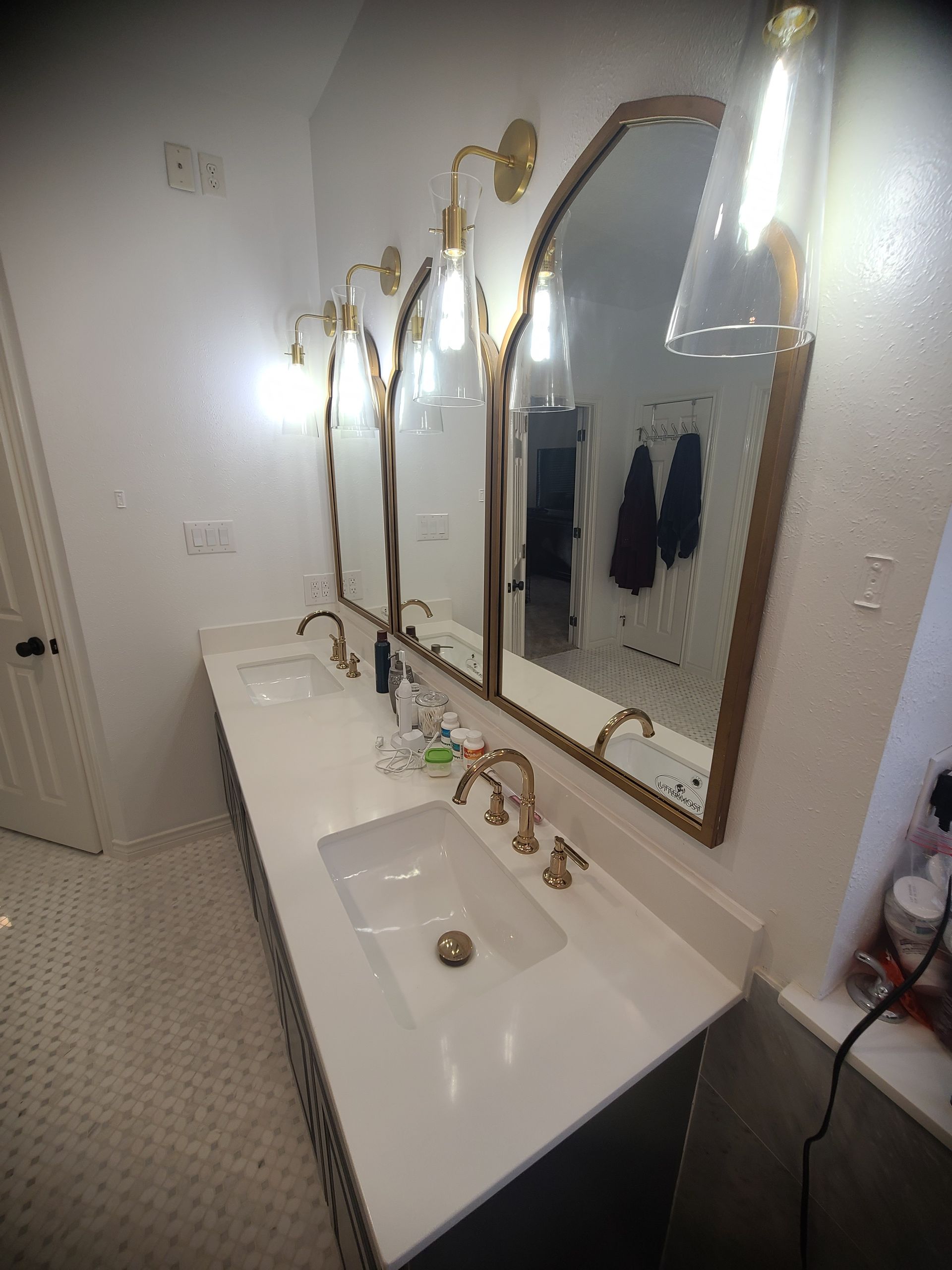 Bathroom with three arched mirrors, gold fixtures, white countertops, and tile flooring.