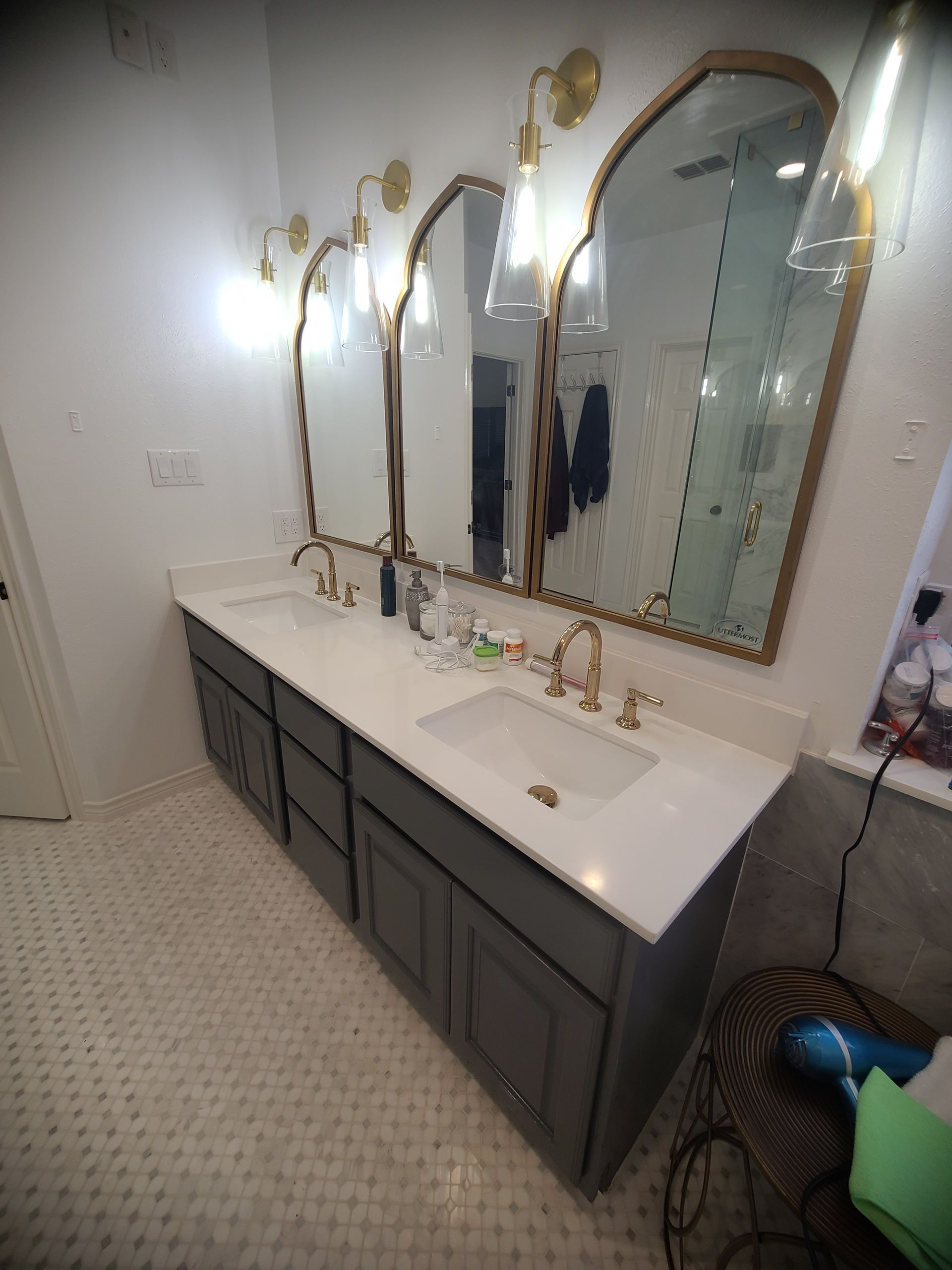 Bathroom with three arched mirrors, gold fixtures, gray cabinets, and white countertop.