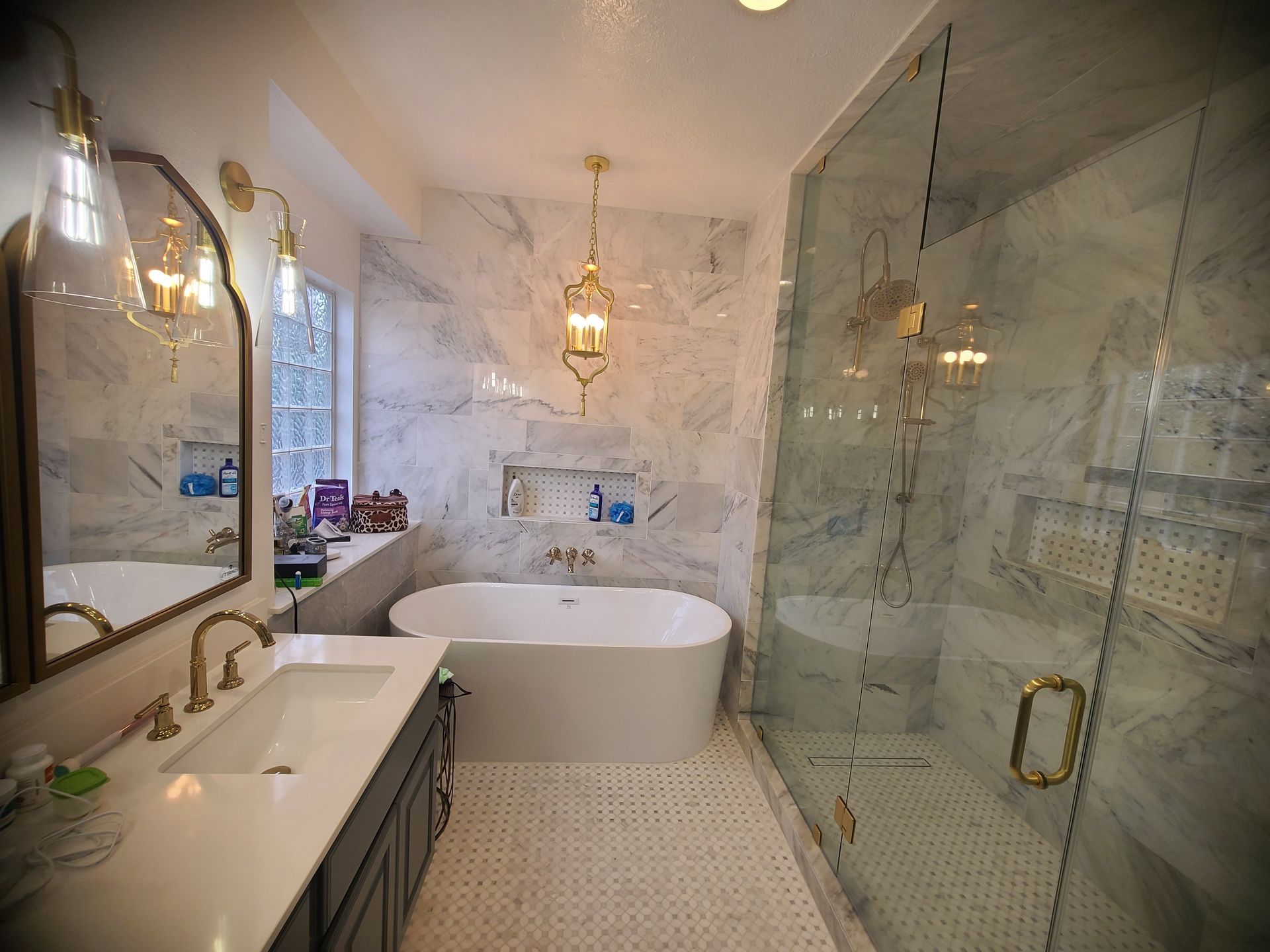 Luxurious bathroom with marble walls, freestanding tub, glass shower, gold fixtures, and ornate chandelier.