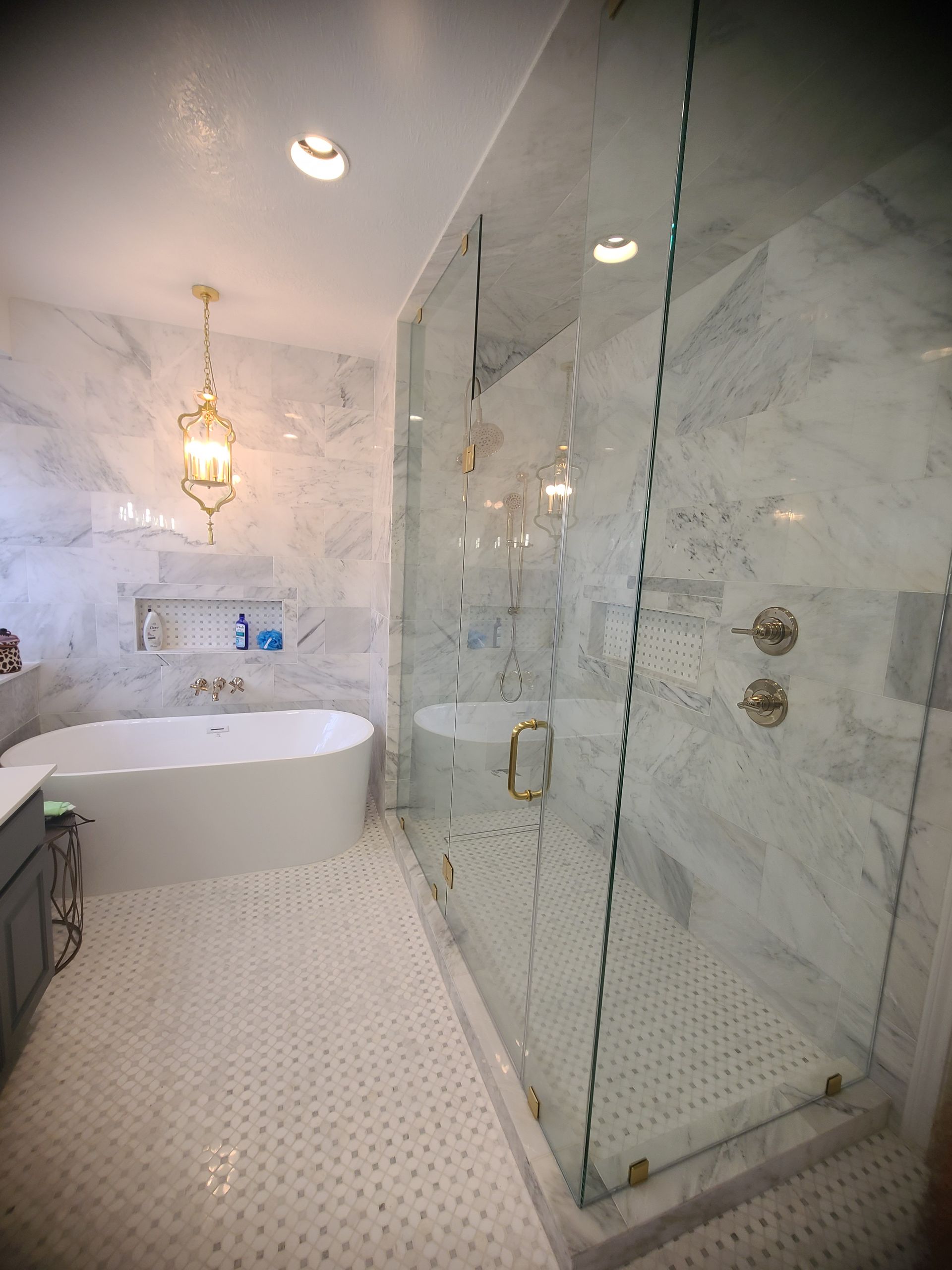 Elegant marble bathroom with glass shower, freestanding tub, gold fixtures.