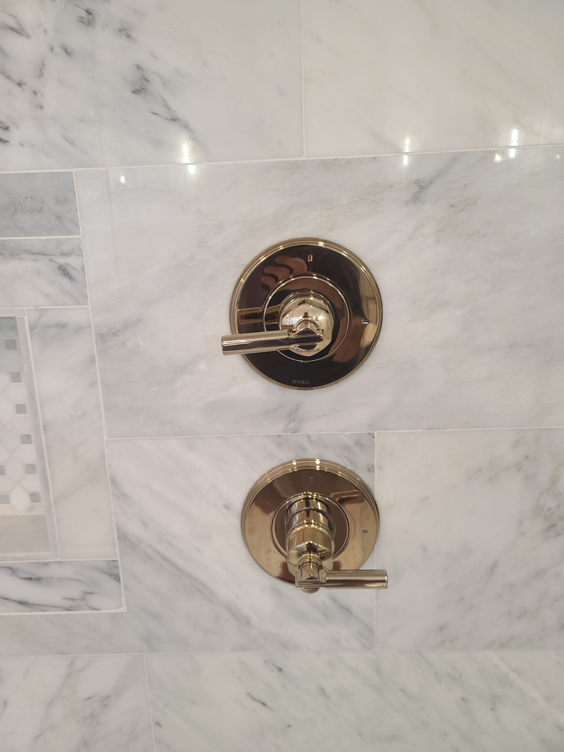 Two gold shower control knobs on a marble tile wall.
