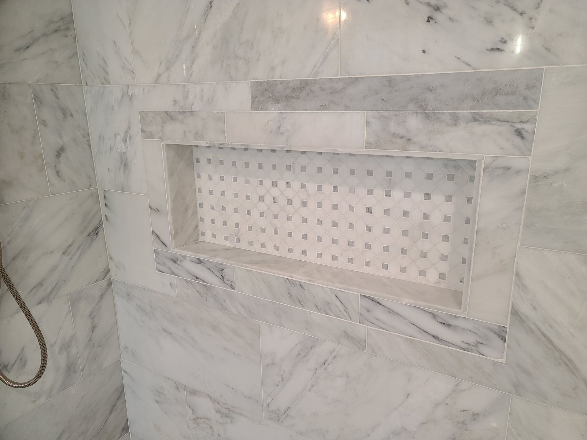 Marble shower niche with white mosaic tile interior, surrounded by large marble tiles.