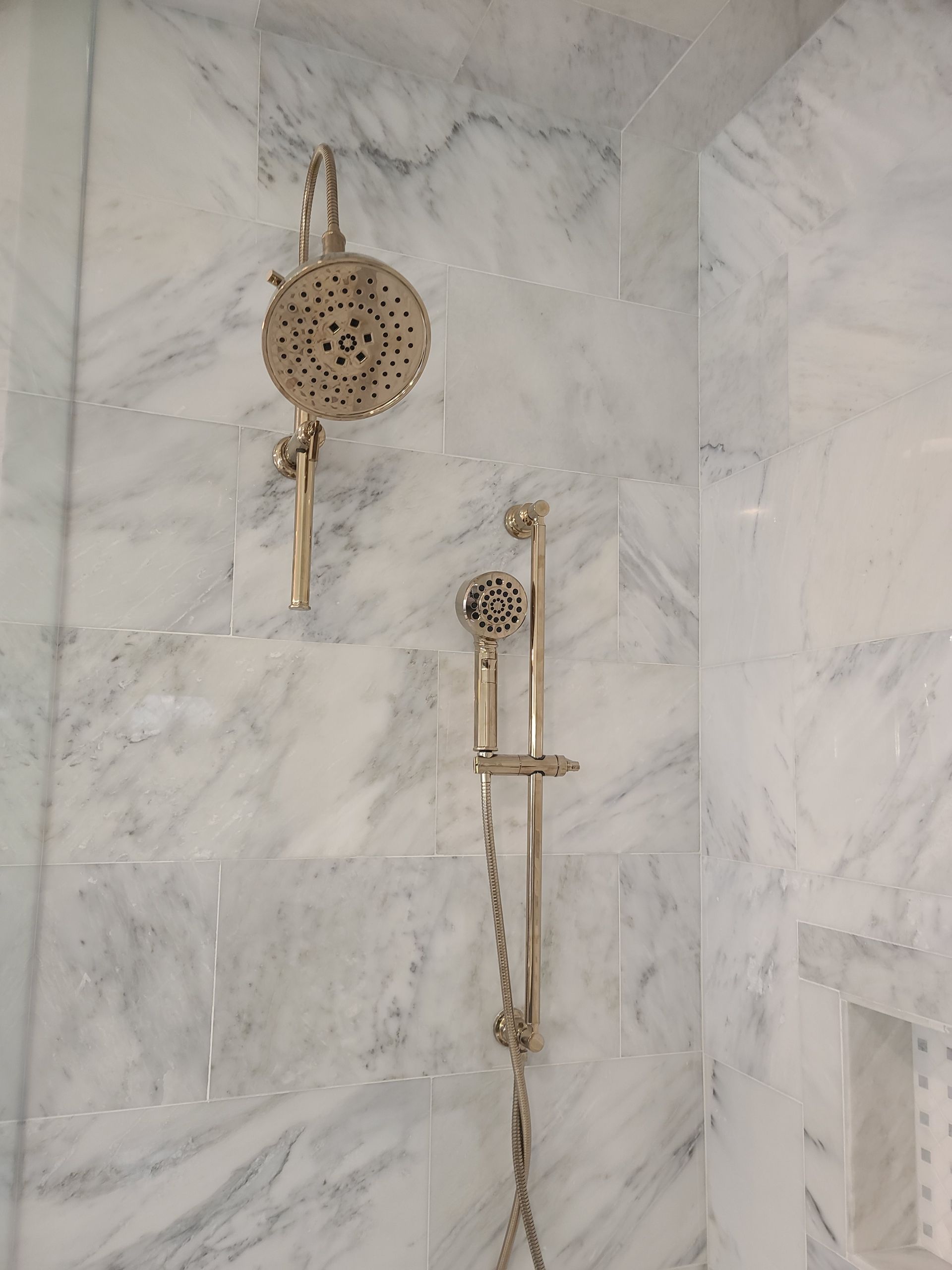 Shower with antique brass showerheads against marble tile.