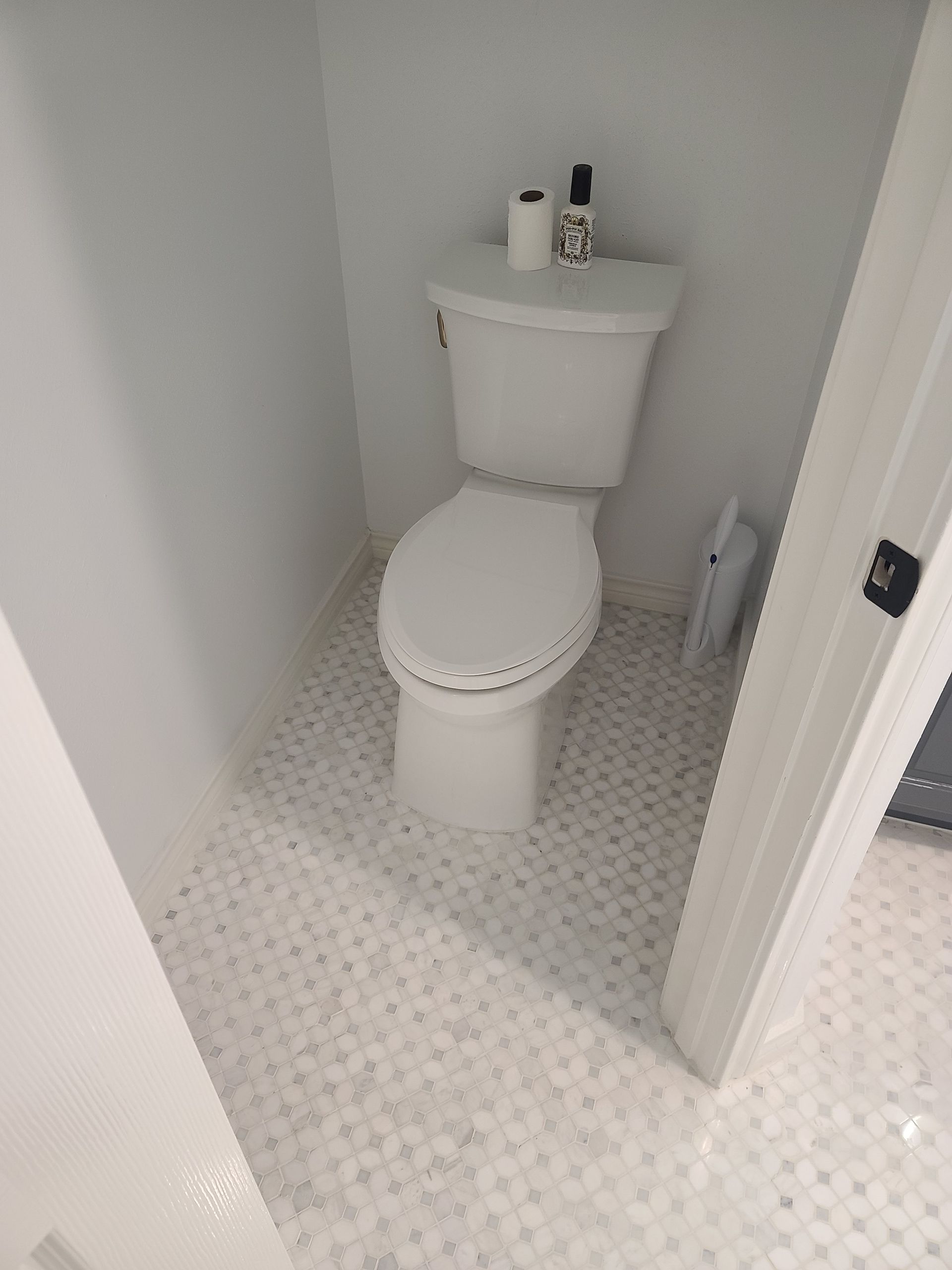 White toilet in a small white bathroom with patterned tile flooring.