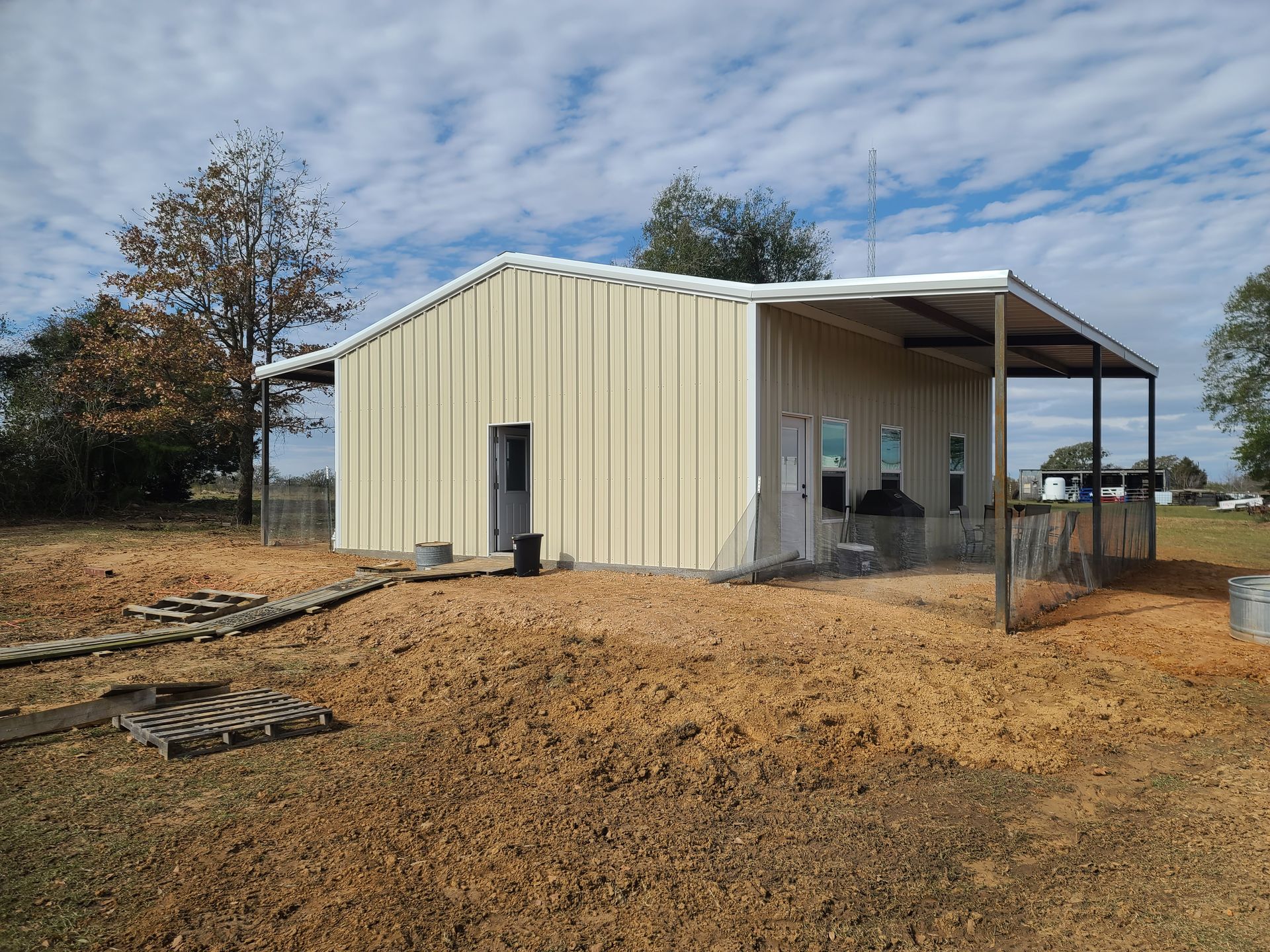 Tan metal building with a covered porch on a brown field under a blue sky.