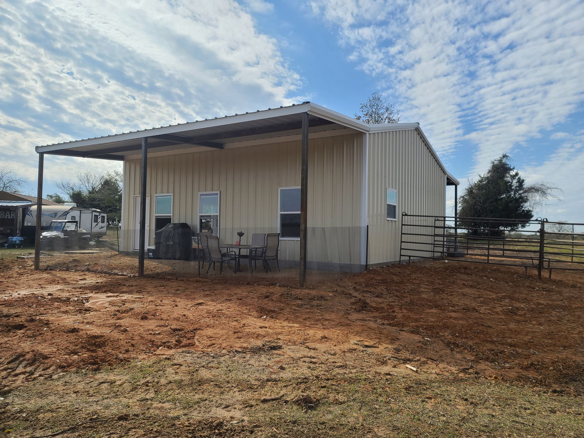 Tan metal building with a covered porch and a bare yard under a cloudy sky.
