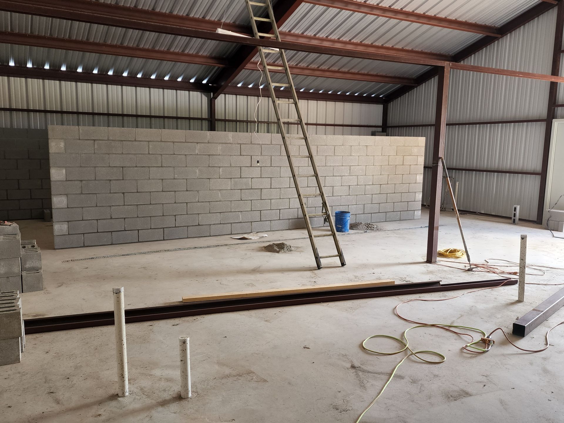 Interior of a warehouse with concrete block walls under construction, ladder, and tools.