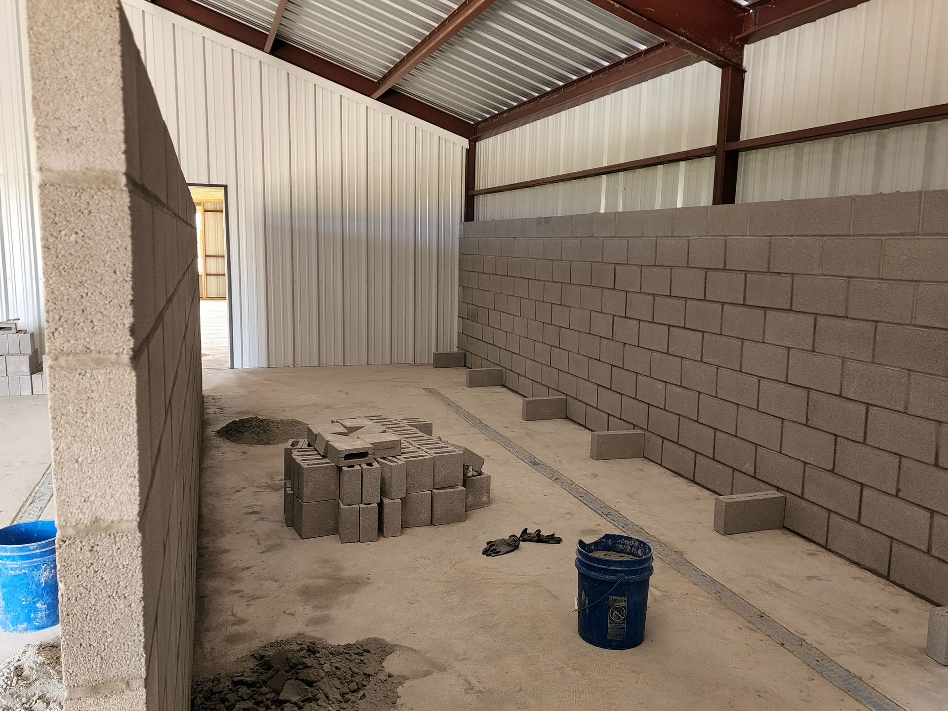 Interior of a building under construction, with cinder block walls, metal beams, and concrete flooring.