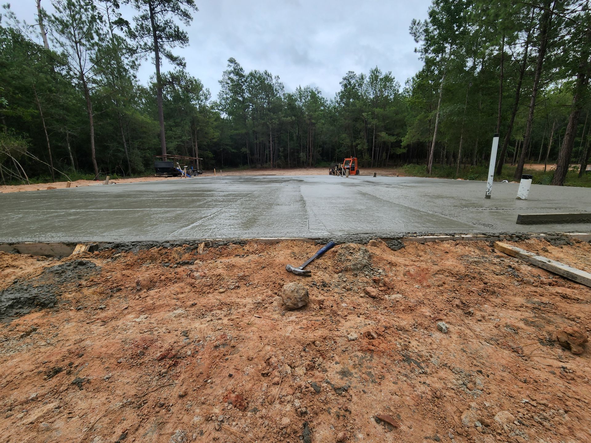 Newly poured concrete slab in a wooded area with construction equipment.