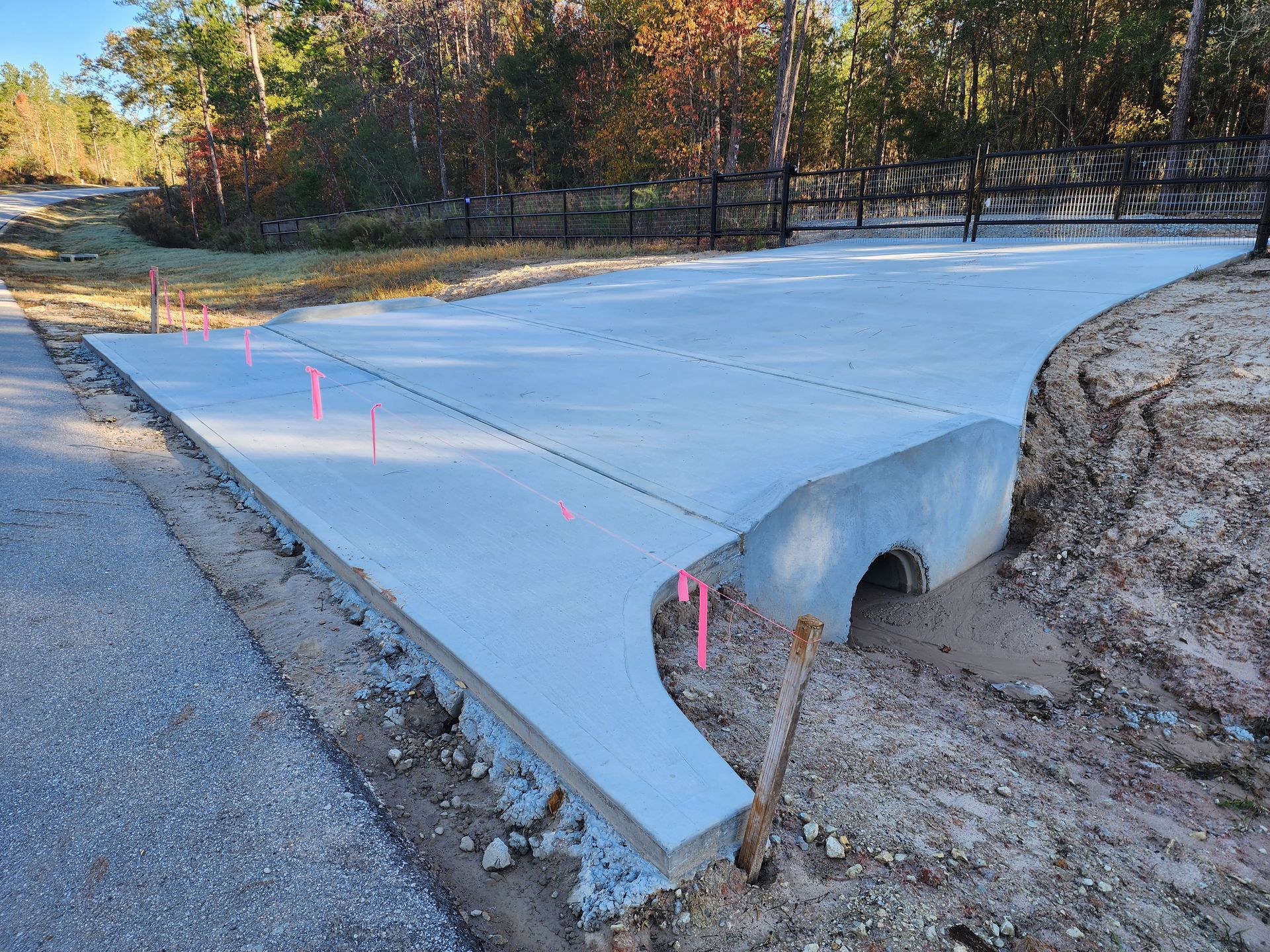 New concrete driveway over a culvert, bordered by gravel and dirt. Pink markers indicate progress.