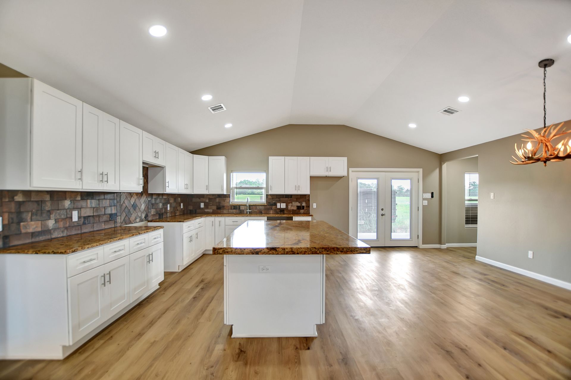 Spacious kitchen with white cabinets, granite countertops, and a large island. Features hardwood floors and a view of the backyard.