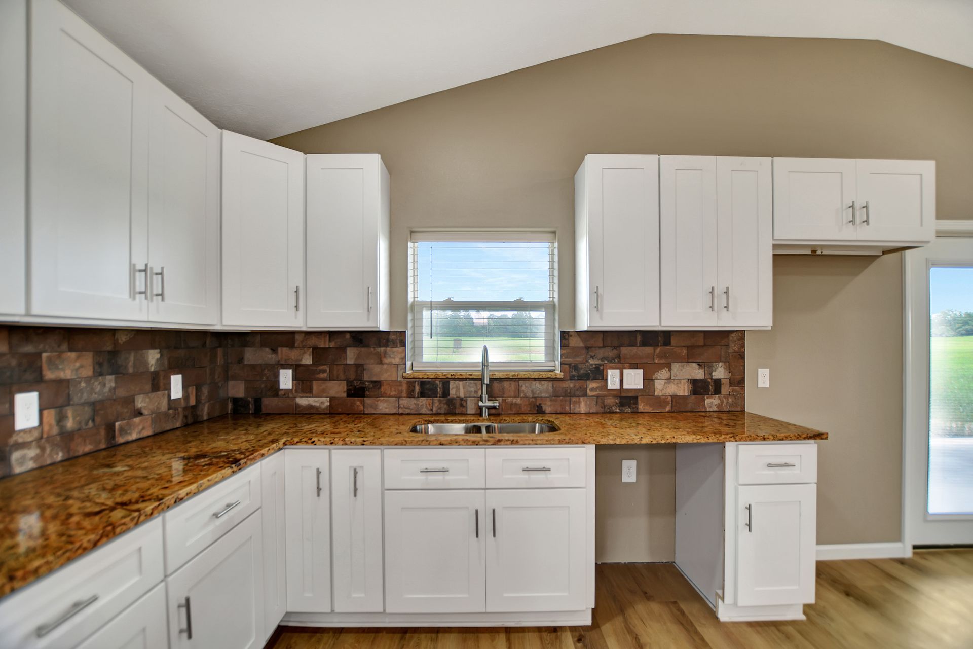 White kitchen cabinets with granite countertops and brick backsplash.