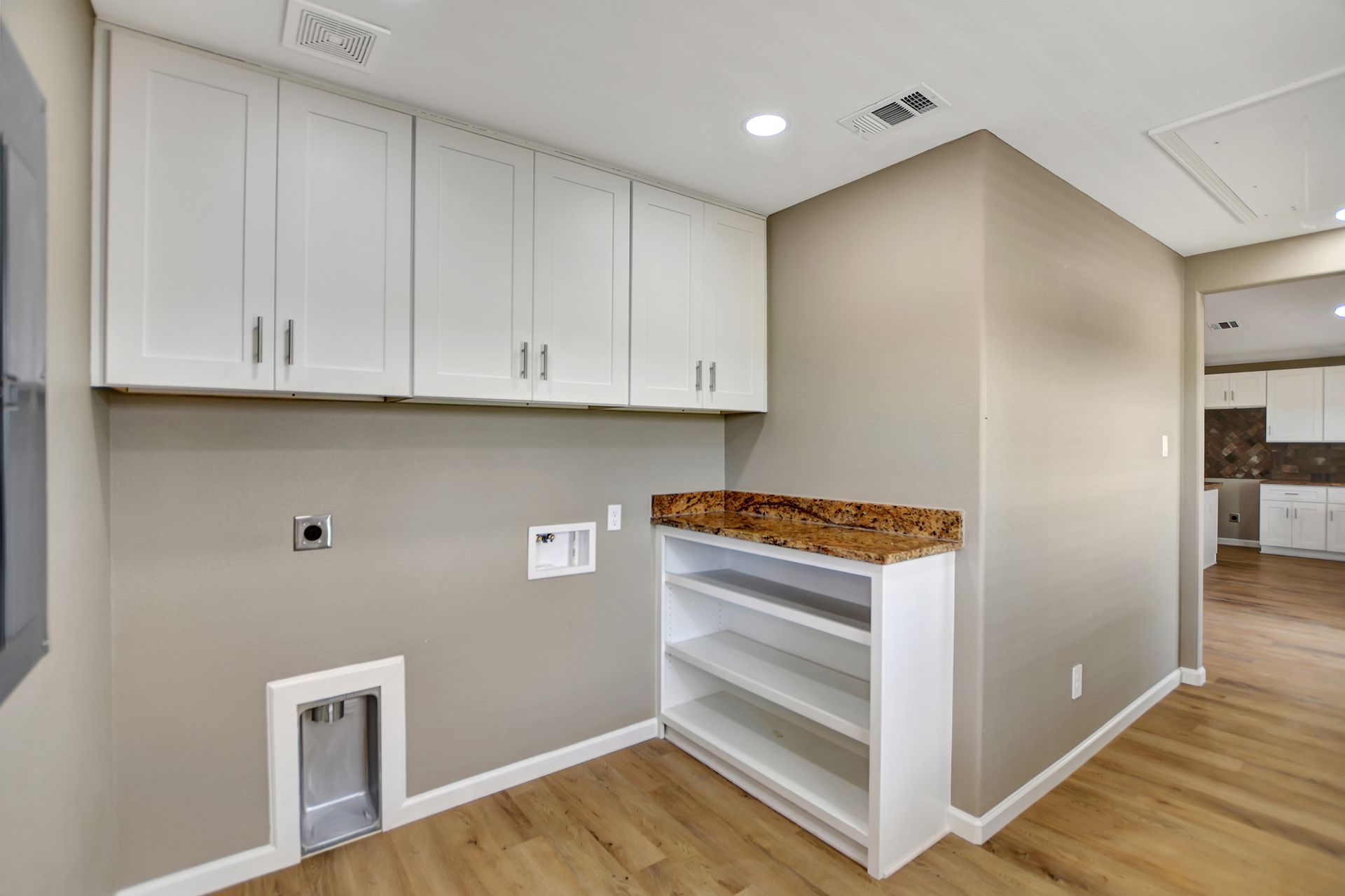 Laundry room with white cabinets, beige walls, and a wood-look floor.