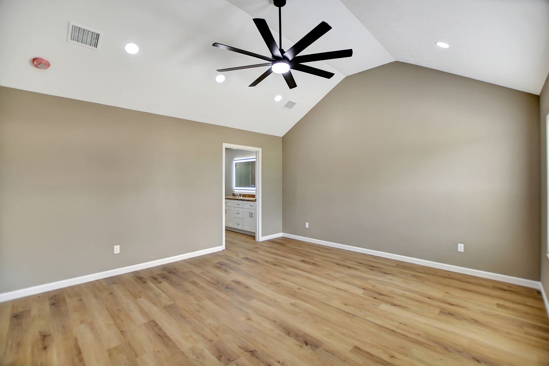 Empty bedroom with vaulted ceiling, wood flooring, and a black ceiling fan.