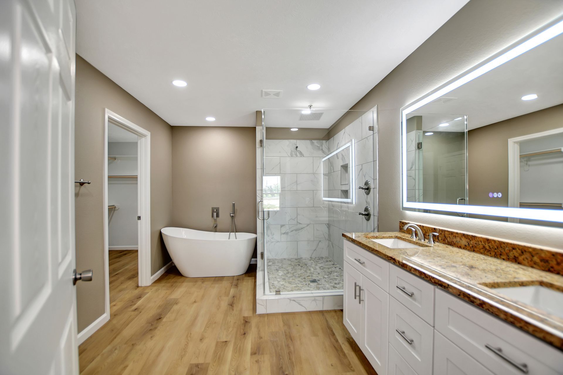 Spacious modern bathroom with a tub, shower, double vanity, and light wood flooring.