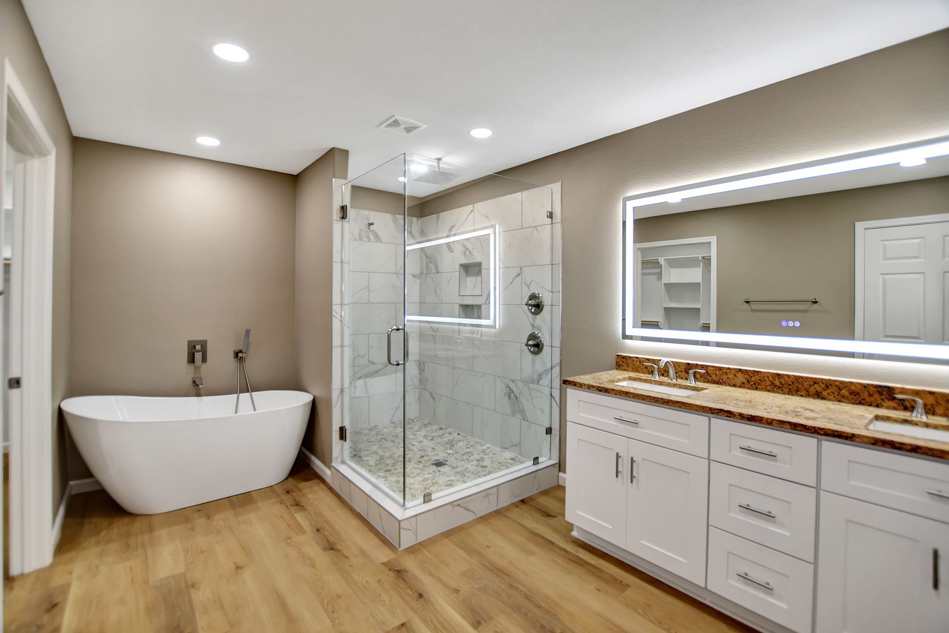 Modern bathroom with a white tub, glass shower, double sink vanity, and light wood flooring.