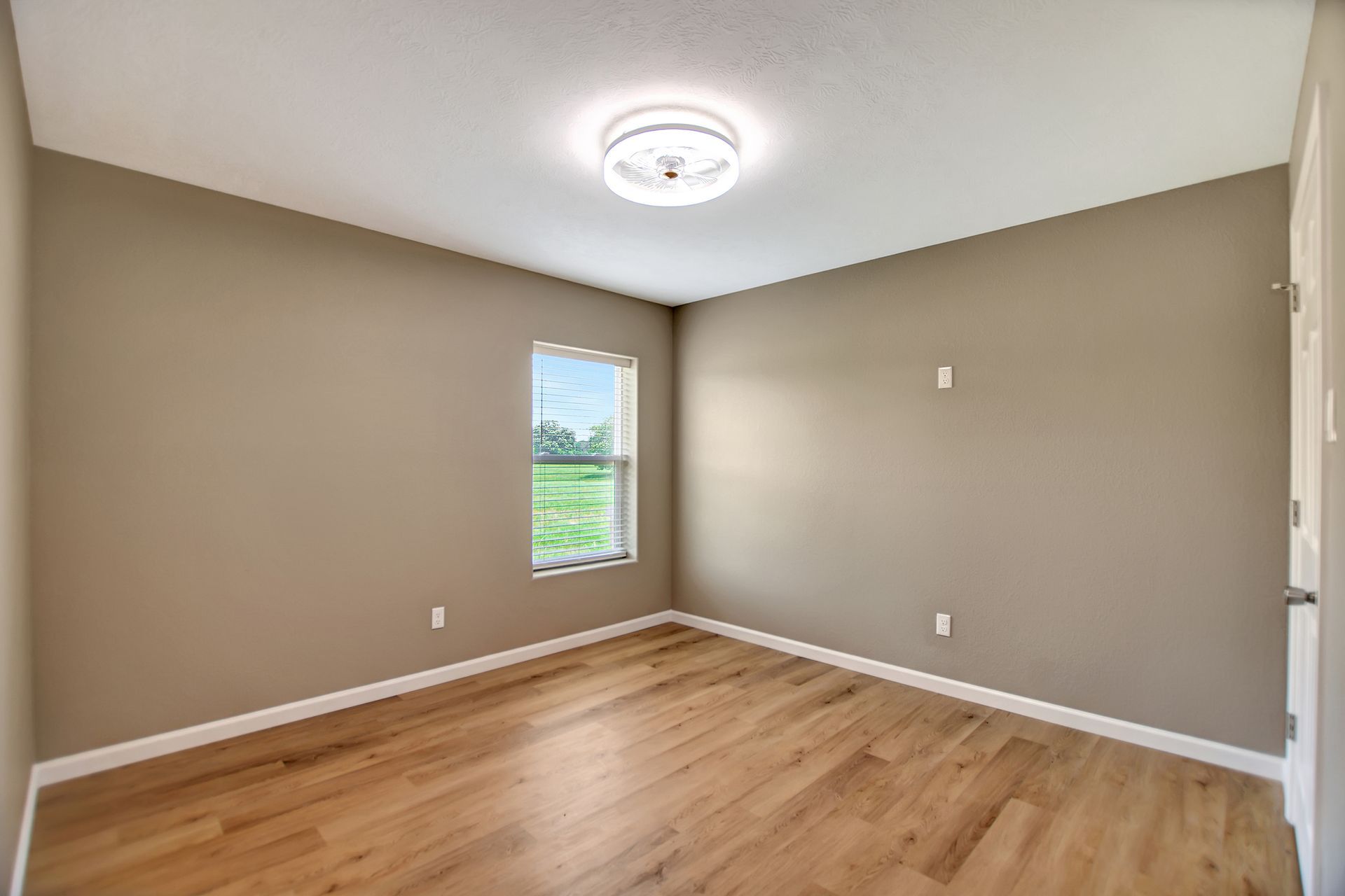 Empty bedroom with tan walls, hardwood floors, a window, and a ceiling light.