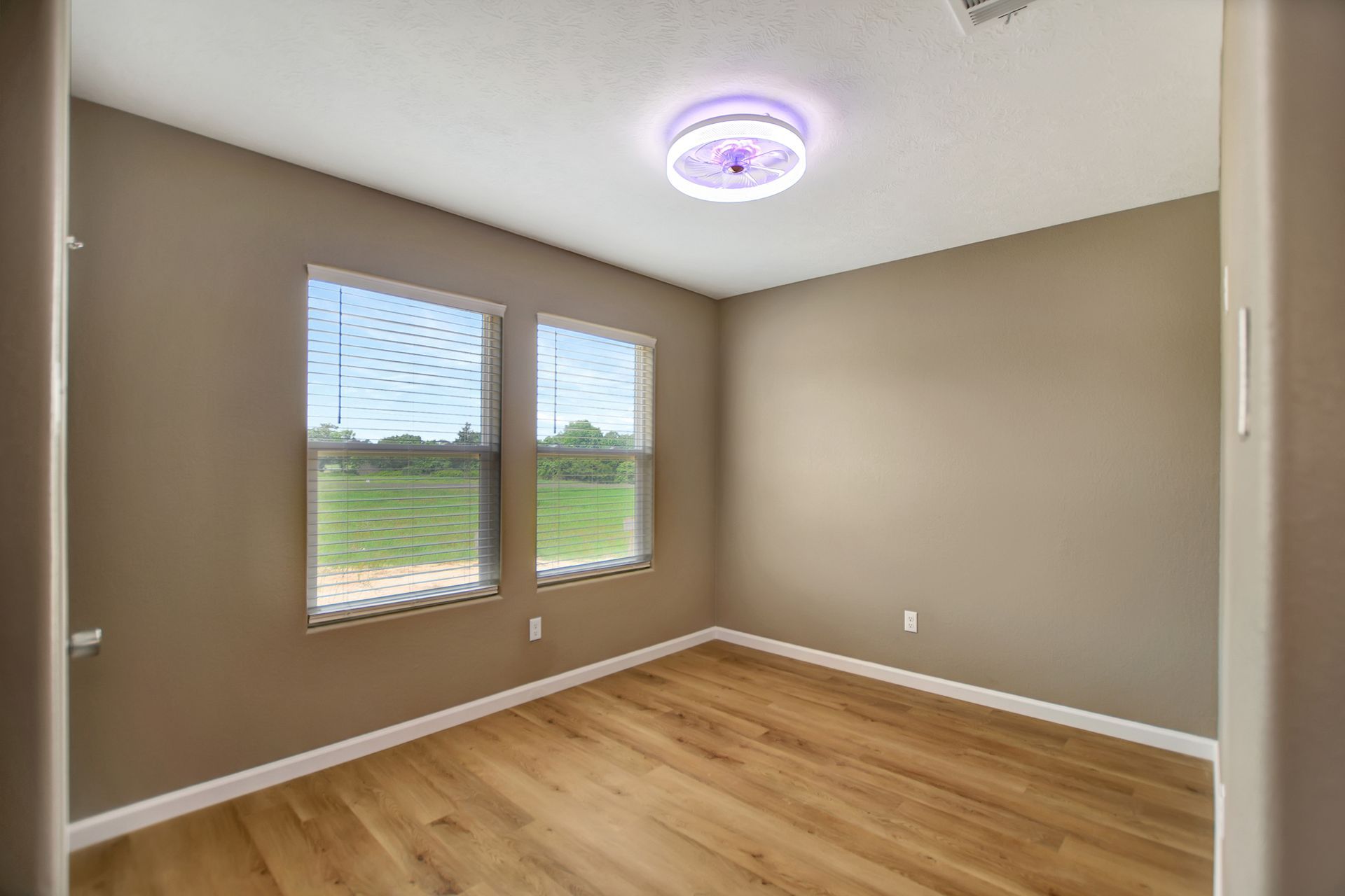 Empty room with two windows, wood floor, beige walls, and a ceiling light.