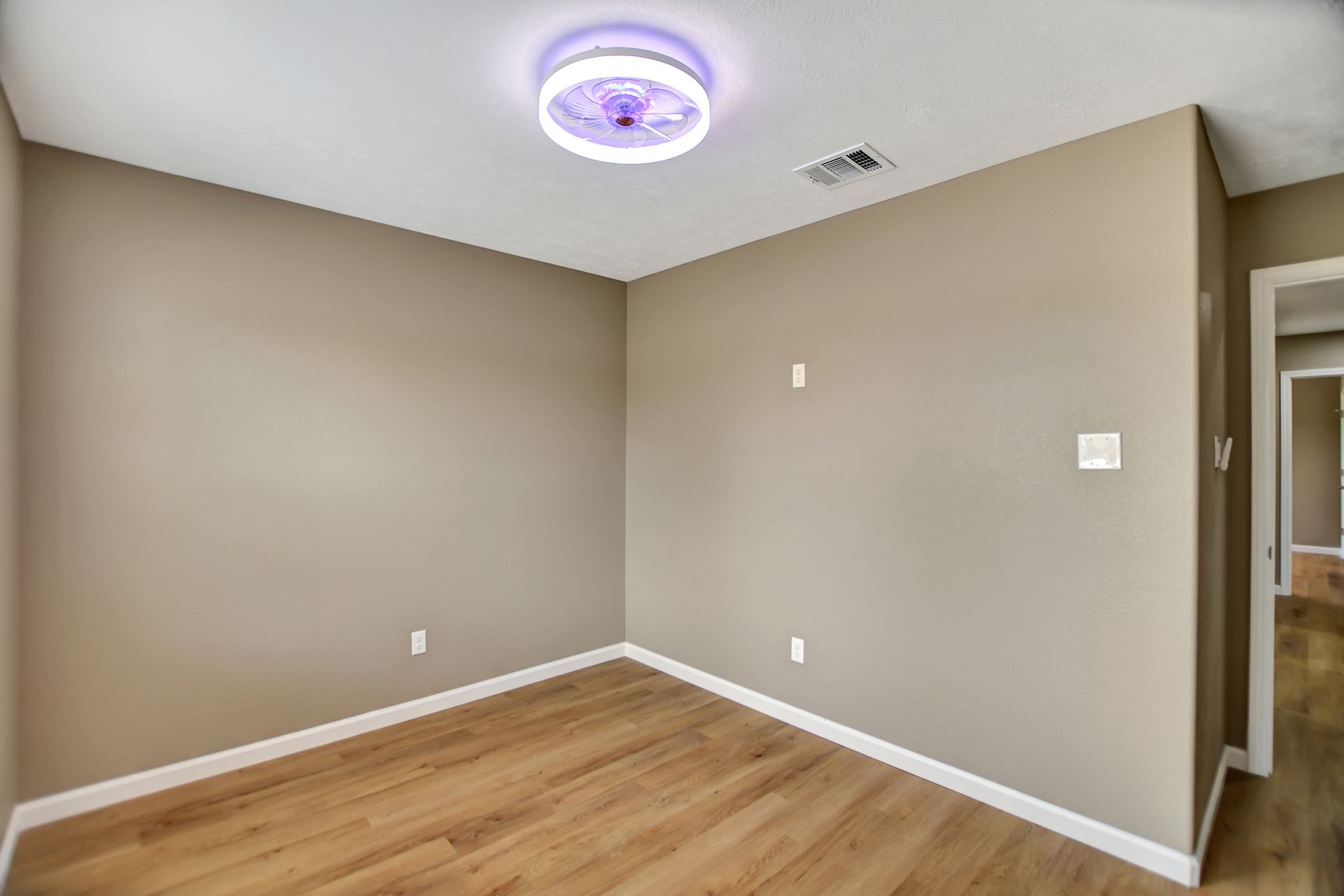Empty room with wood-look flooring, beige walls, and a ceiling light.