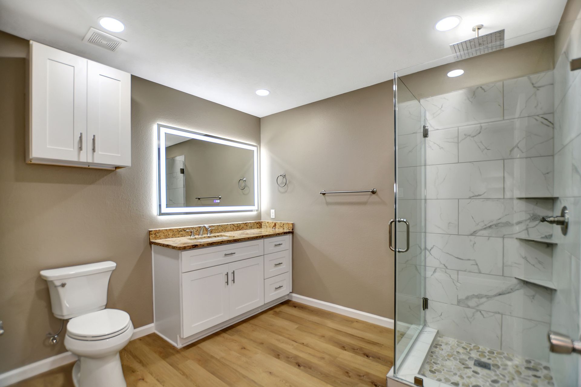 Modern bathroom with white cabinets, marble shower, and wood-look flooring.