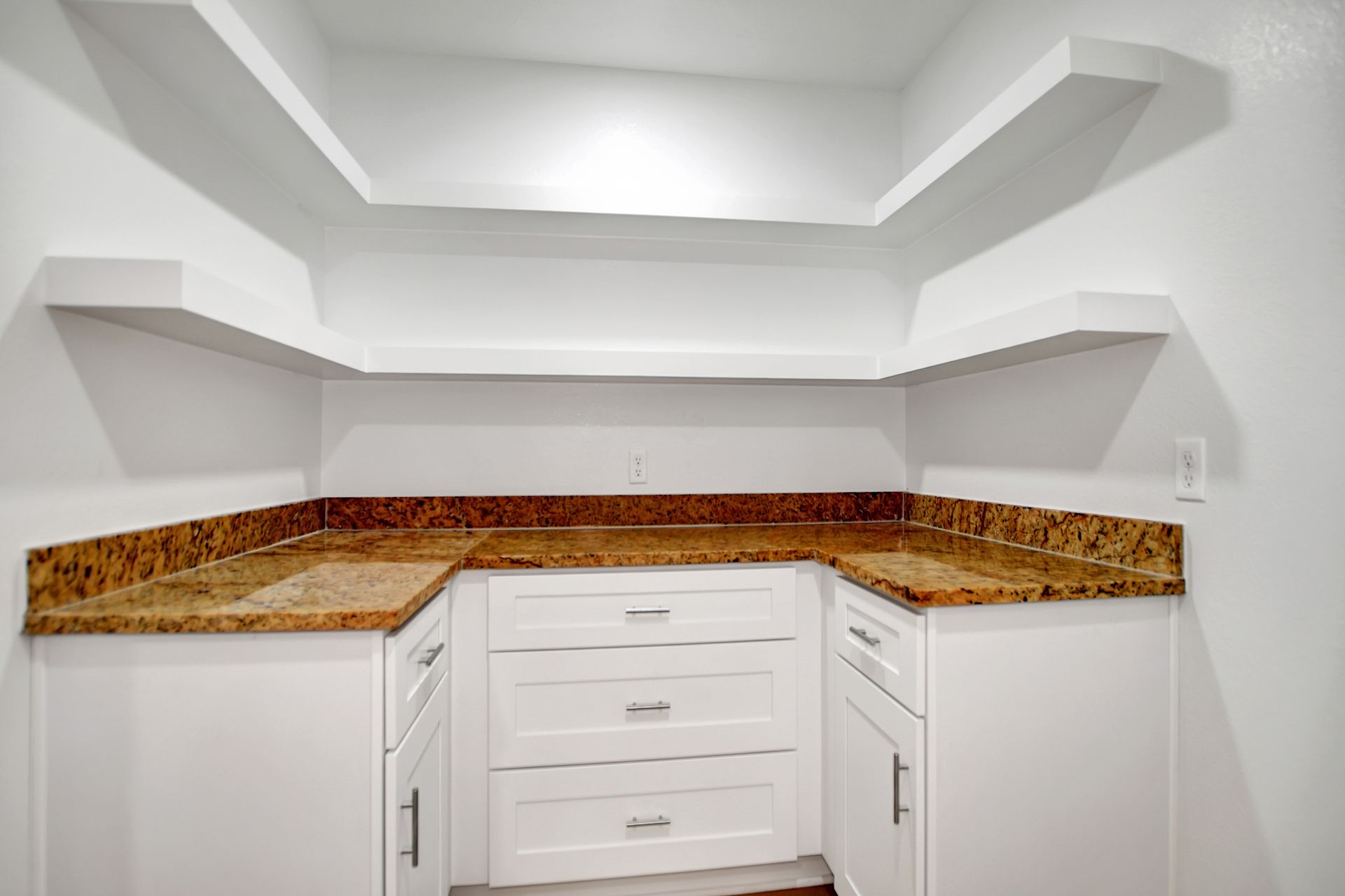 White cabinets and shelves in a corner with a tan countertop.