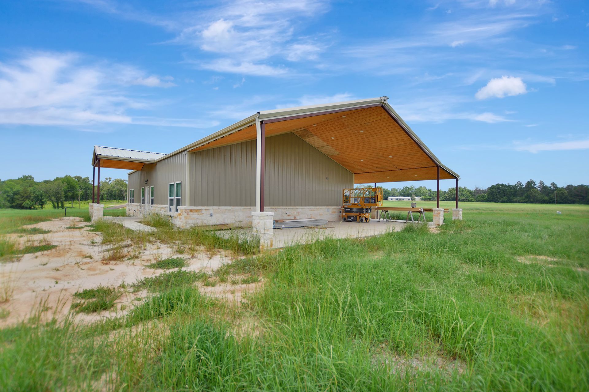 Tan metal building with a covered porch on a grassy plain under a blue sky.