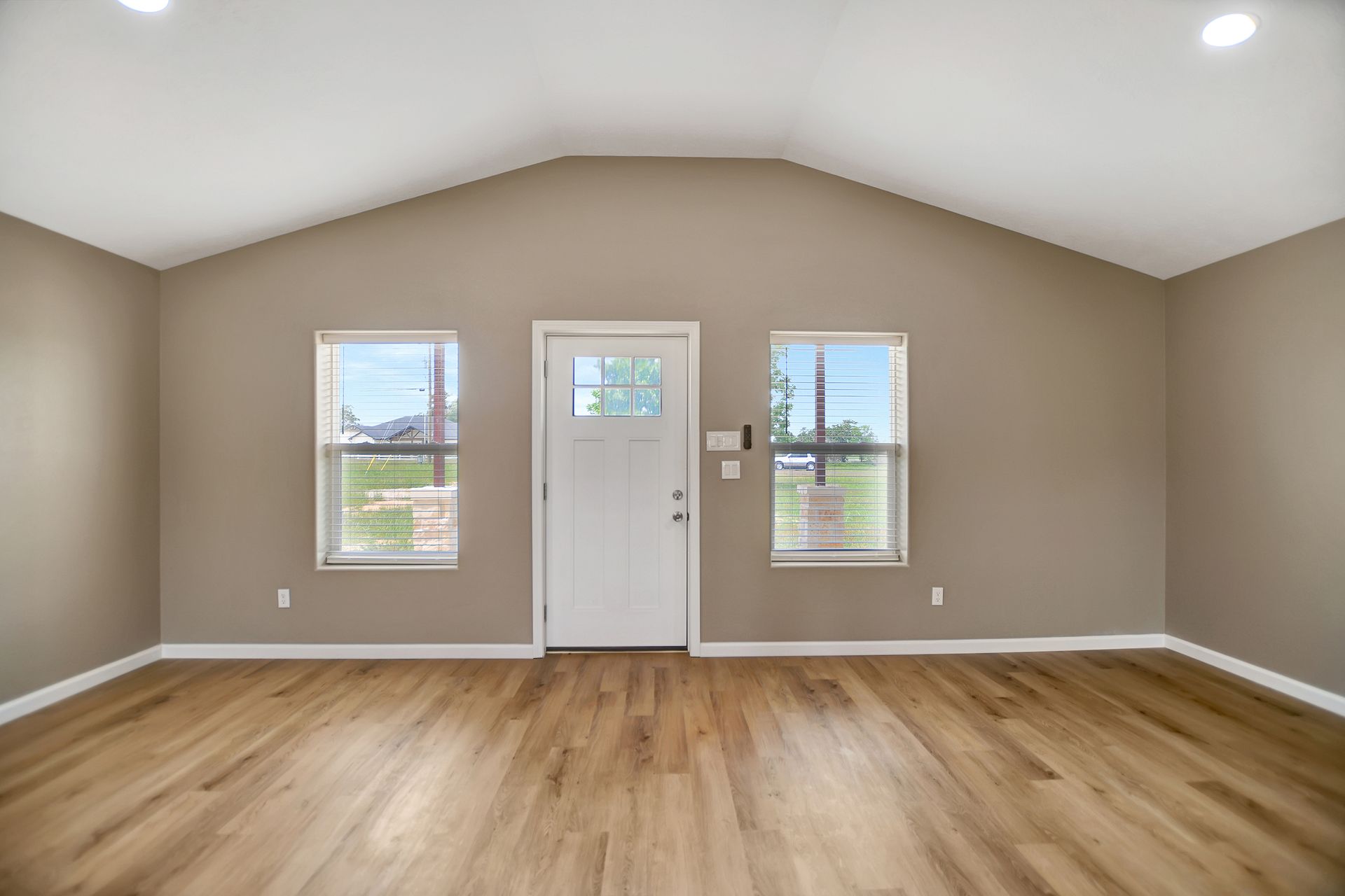 Interior view of a room with hardwood floors, windows, and a white door; beige walls.