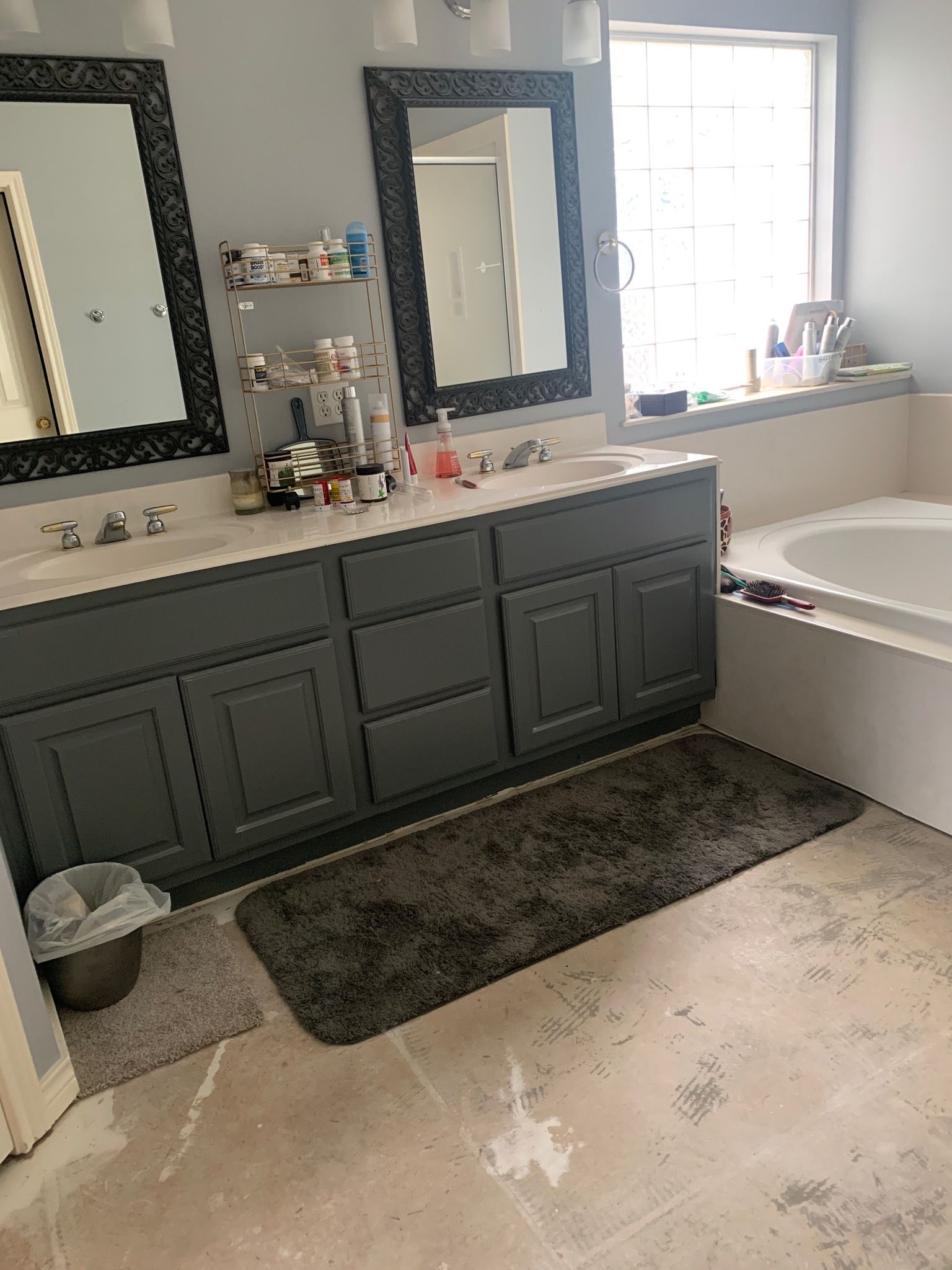 Bathroom with gray vanity, two mirrors, a bathtub, and a dark gray rug on the floor.