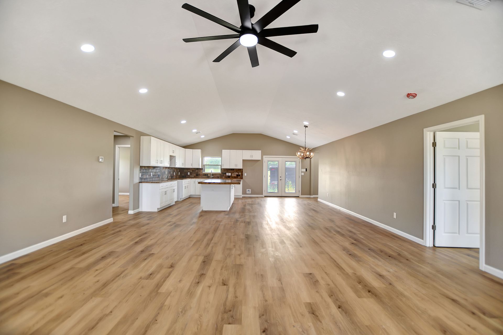 Spacious open-concept living area with light wood floors, kitchen island, and a vaulted ceiling.