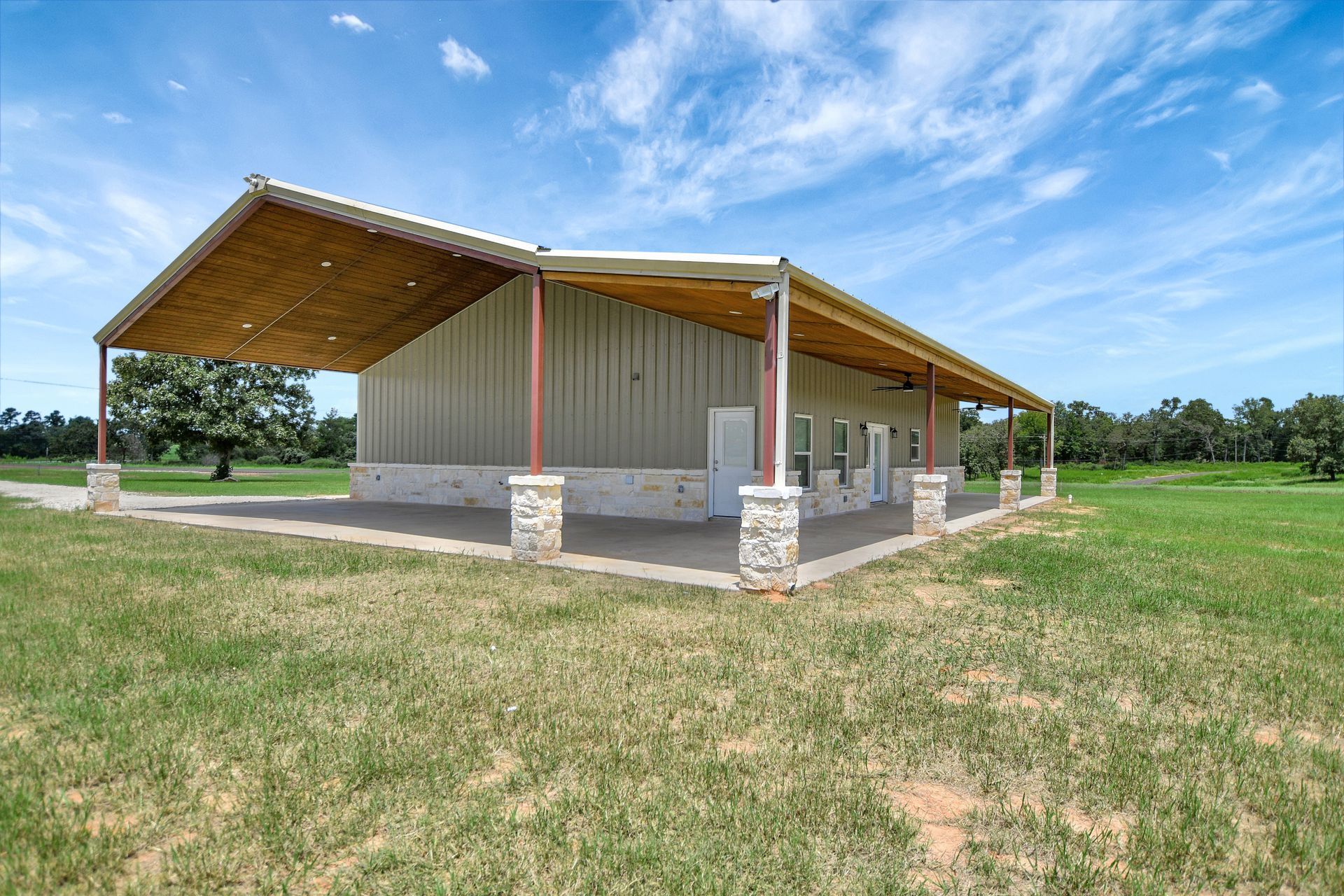 Metal-sided building with a covered porch on a grassy field under a blue sky.