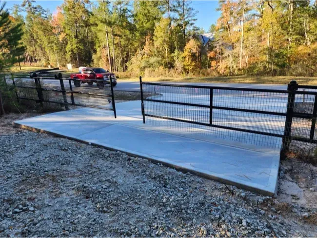 A red truck is parked in a gravel lot next to a fence.