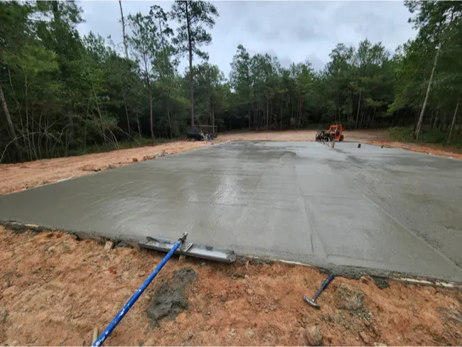 A tractor is driving down a dirt road next to a concrete floor.