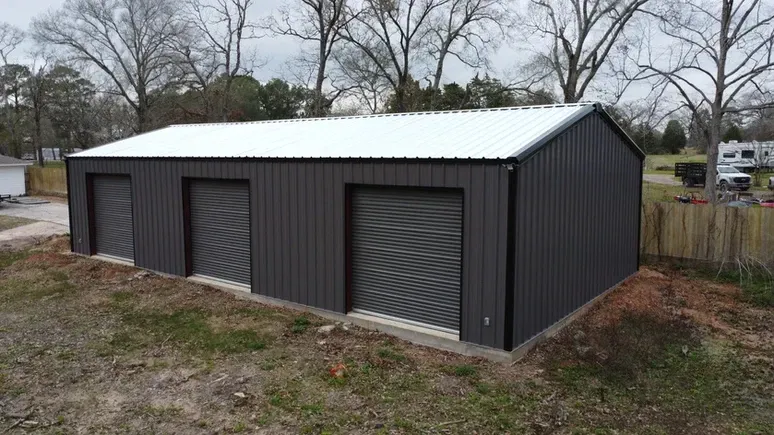 A black metal garage with three garage doors and a white roof.