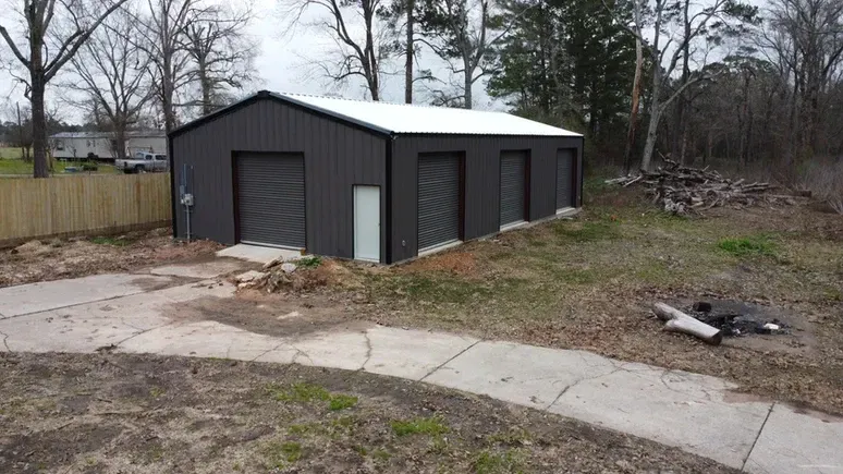 A black garage with a white roof is in the middle of a yard.