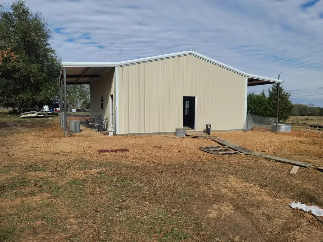 A white metal building is sitting in the middle of a field.
