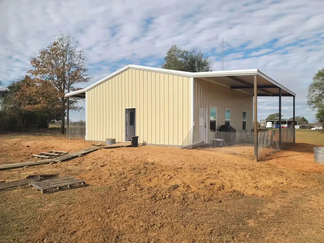 A metal building with a porch is sitting in the middle of a dirt field.