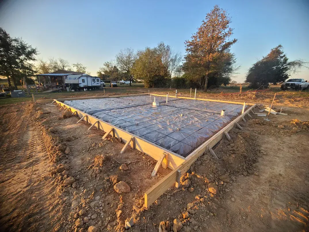 A concrete foundation is being built in a dirt field.