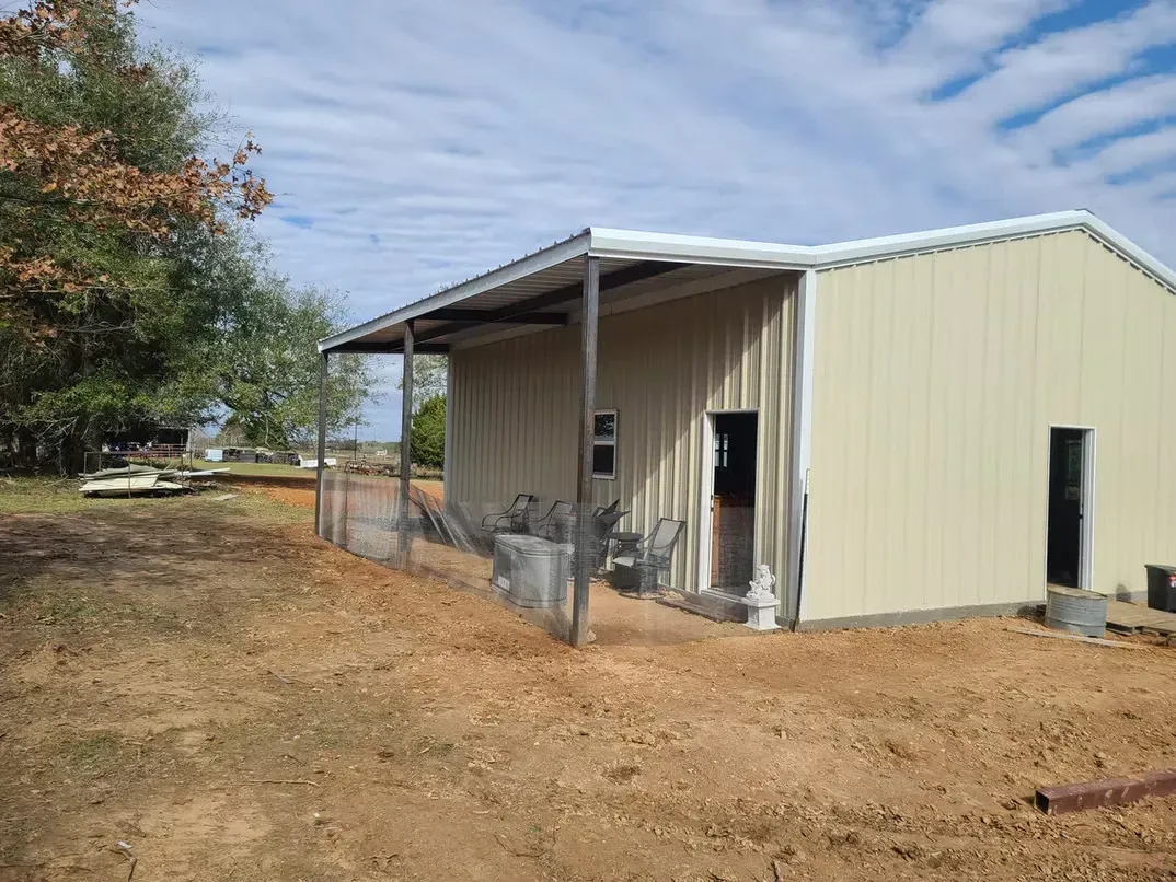 A metal building with a porch is sitting in the middle of a dirt field.